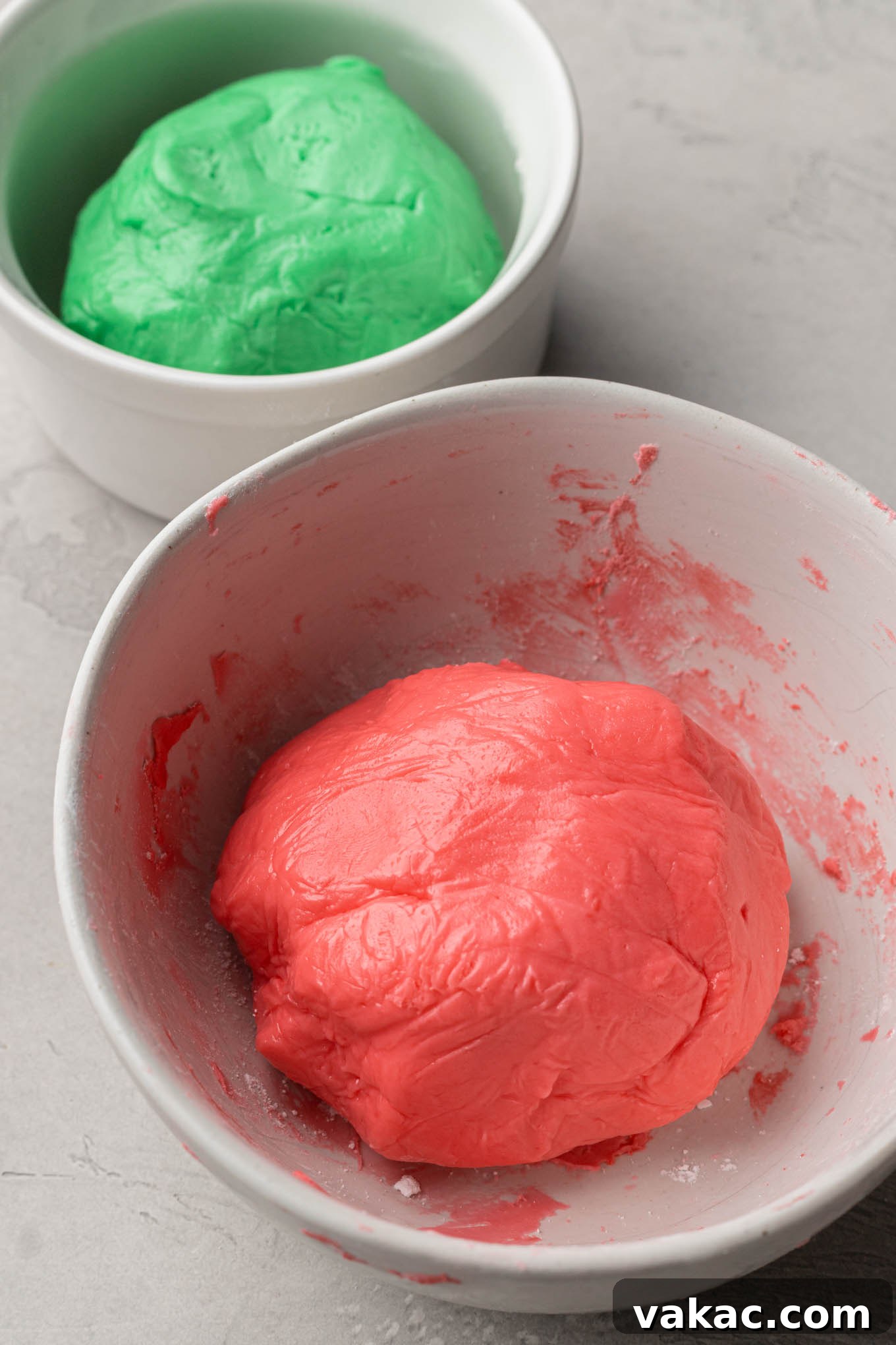Separate mixing bowls containing portions of homemade mint mixture, dyed vibrant red and green with gel food coloring, ready for shaping.