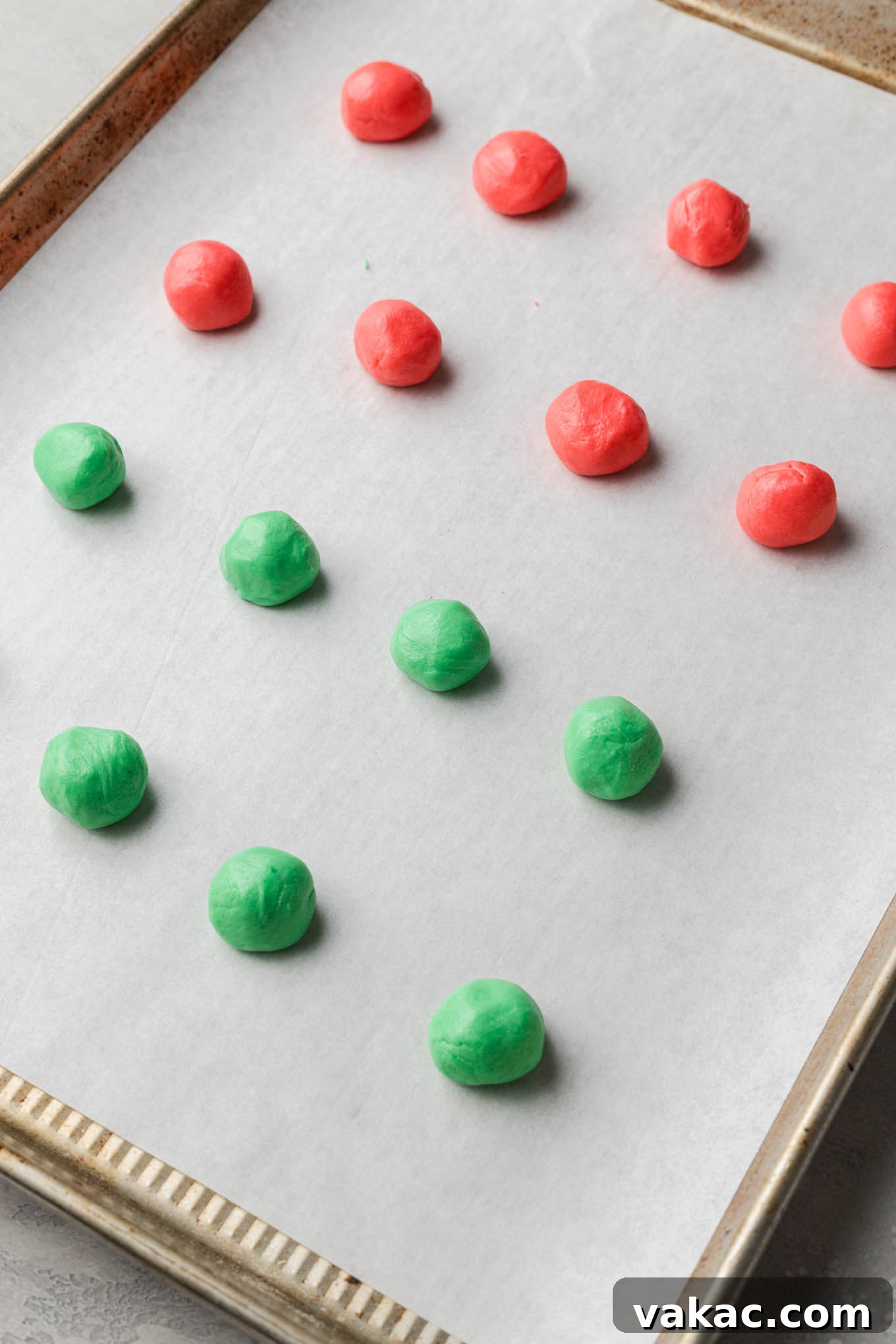 Small, round red and green Christmas cream cheese mints neatly arranged on a parchment paper-lined baking sheet, showing their characteristic fork indentations.