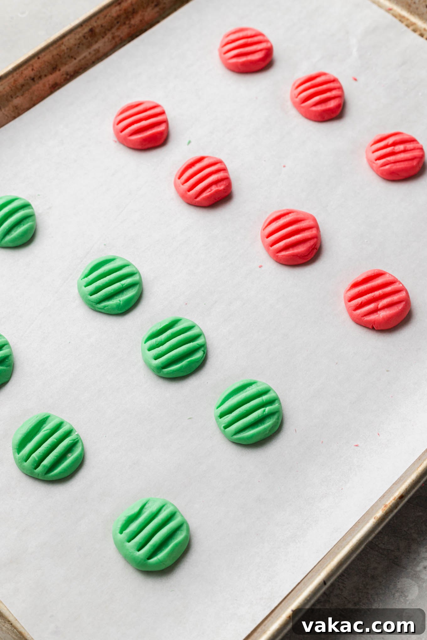 Rows of freshly made red and green cream cheese mints drying on a parchment paper-lined baking sheet, preparing for their final set.