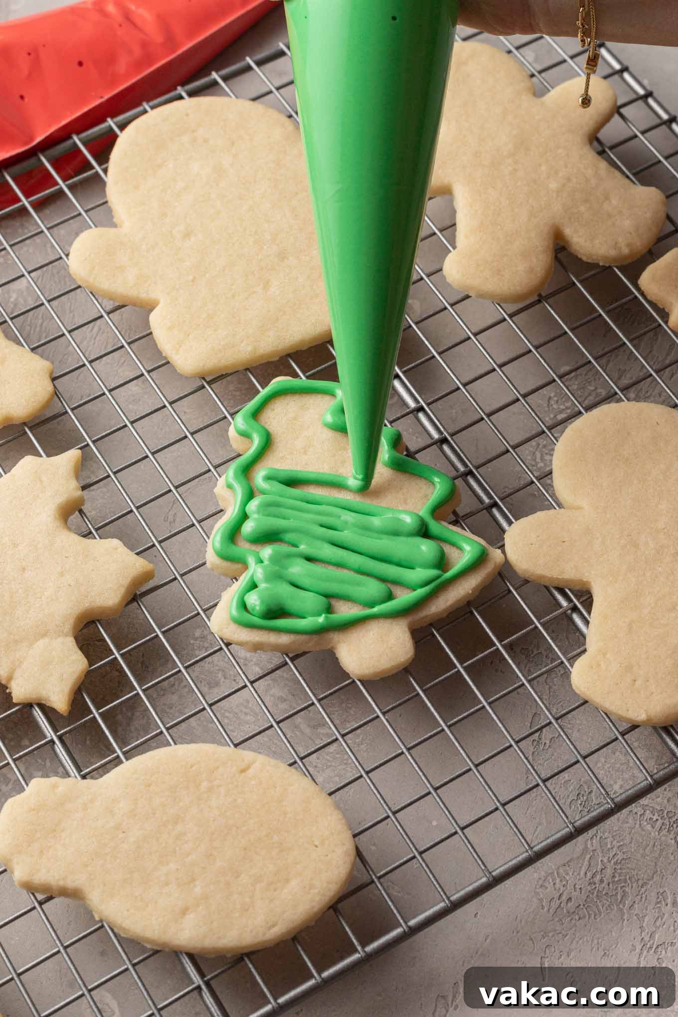 An outlined sugar cookie shaped like a tree being filled with green royal icing.