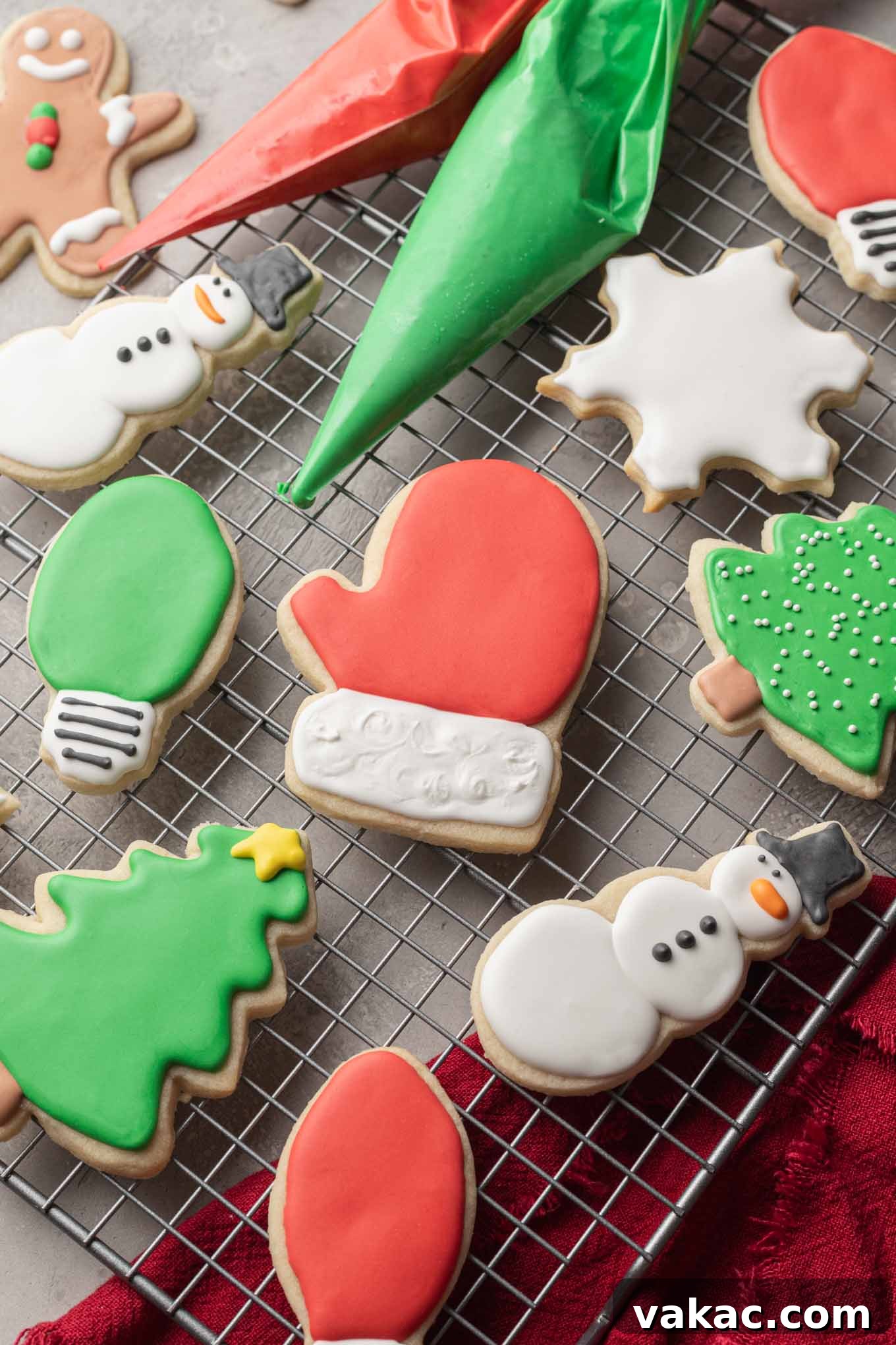 Christmas themed sugar cookies on a wire cooling rack. A bag of red and green icing are laying on the cooling rack with the cookies.