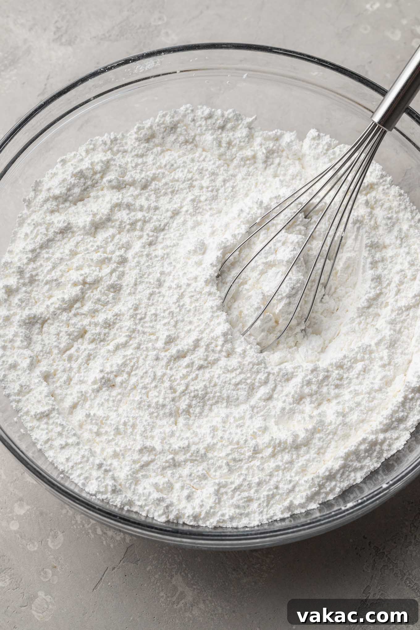 Meringue powder and powdered sugar whisked together in a glass mixing bowl.