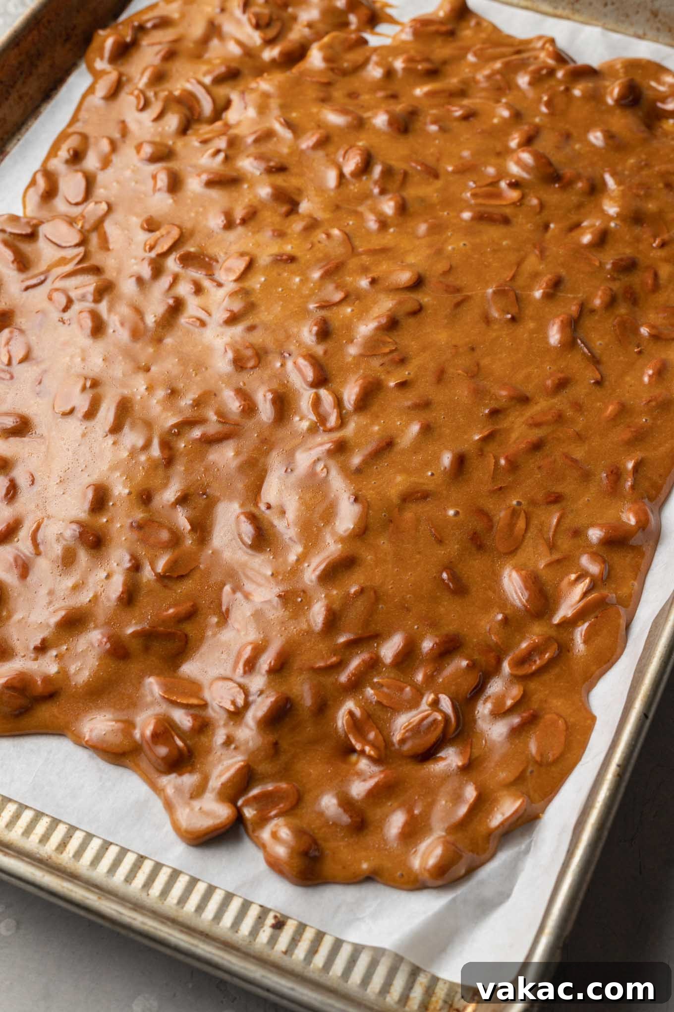 Sweet Peanut Crunch 7 An overhead view of hot peanut brittle spread over a parchment paper-lined cookie sheet.