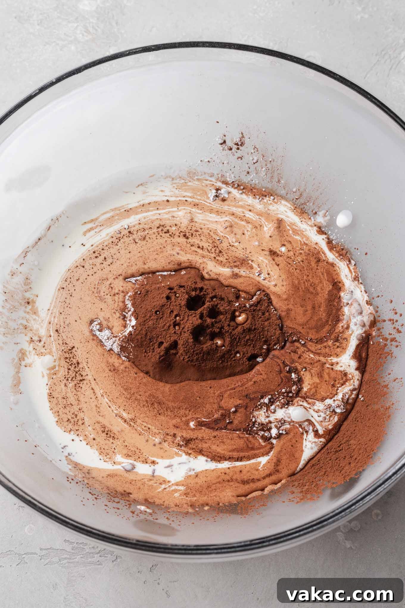 Velvet Chocolate Whip 5 A glass mixing bowl with heavy cream, powdered sugar, cocoa powder, and vanilla extract.