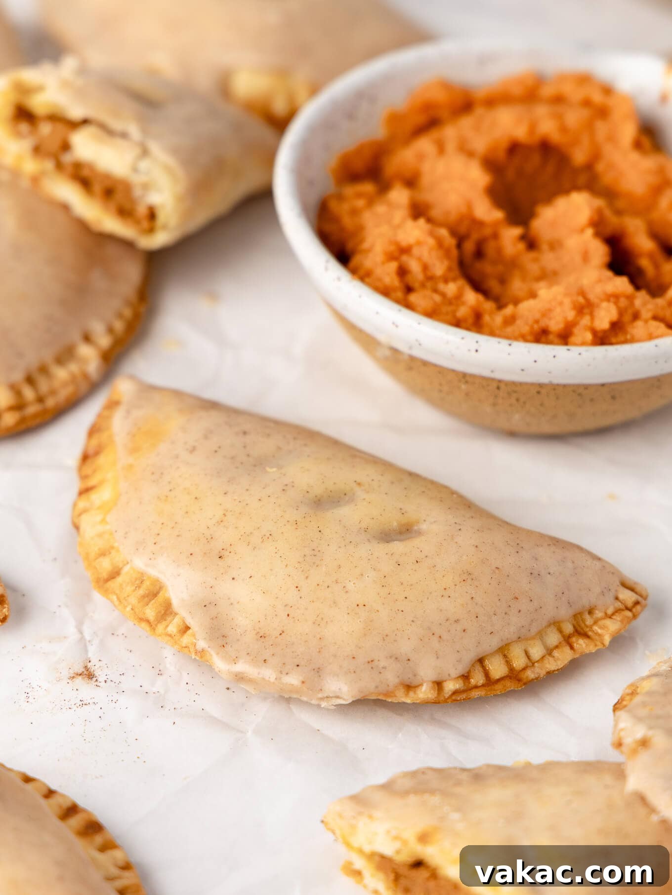 Autumn Pumpkin Pockets 11 A perfectly glazed pumpkin hand pie resting beside a small bowl of creamy pumpkin puree, highlighting its key ingredient.