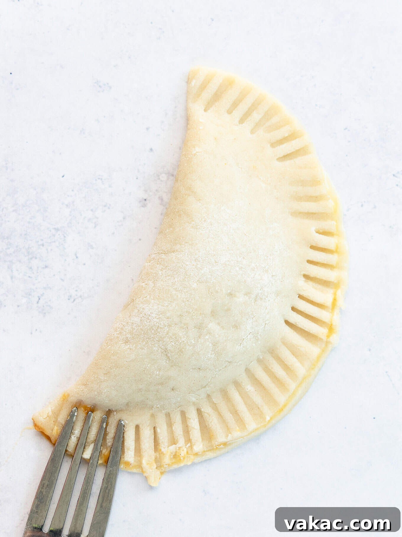 Autumn Pumpkin Pockets 7 A freshly folded pumpkin hand pie, its edges expertly crimped shut with a fork, ready for baking.