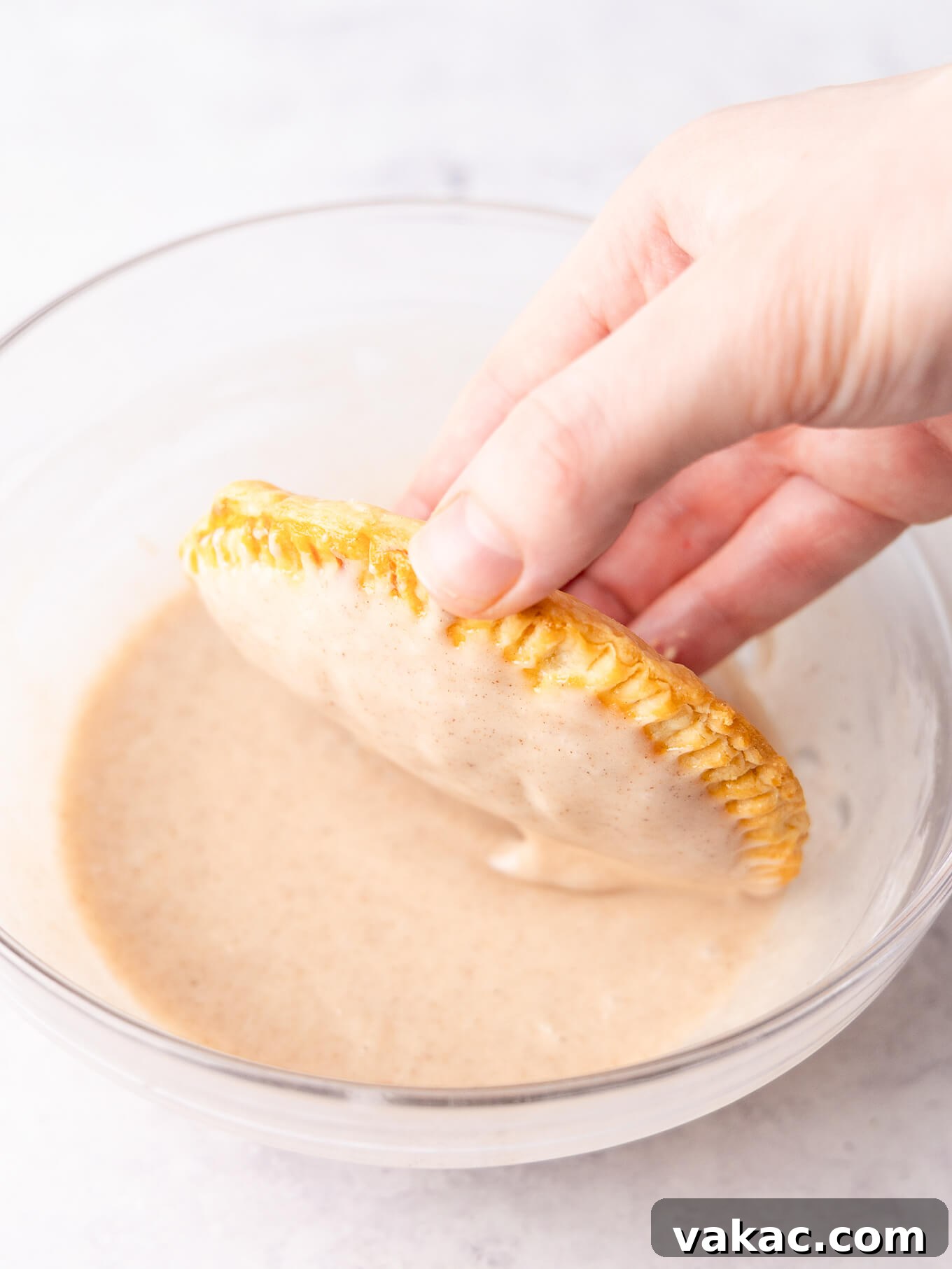 Autumn Pumpkin Pockets 9 A freshly baked pumpkin hand pie being dipped into a smooth, spiced glaze, ensuring full coverage.