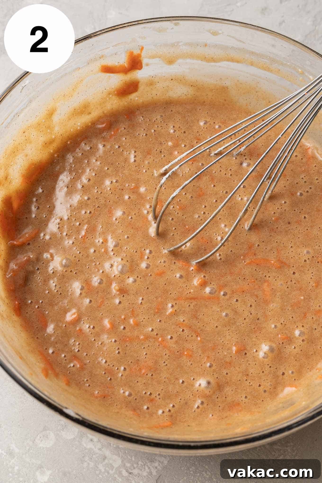 Decadent Spiced Carrot Cheesecake 5 An overhead view of carrot cake batter in a glass mixing bowl with a whisk.