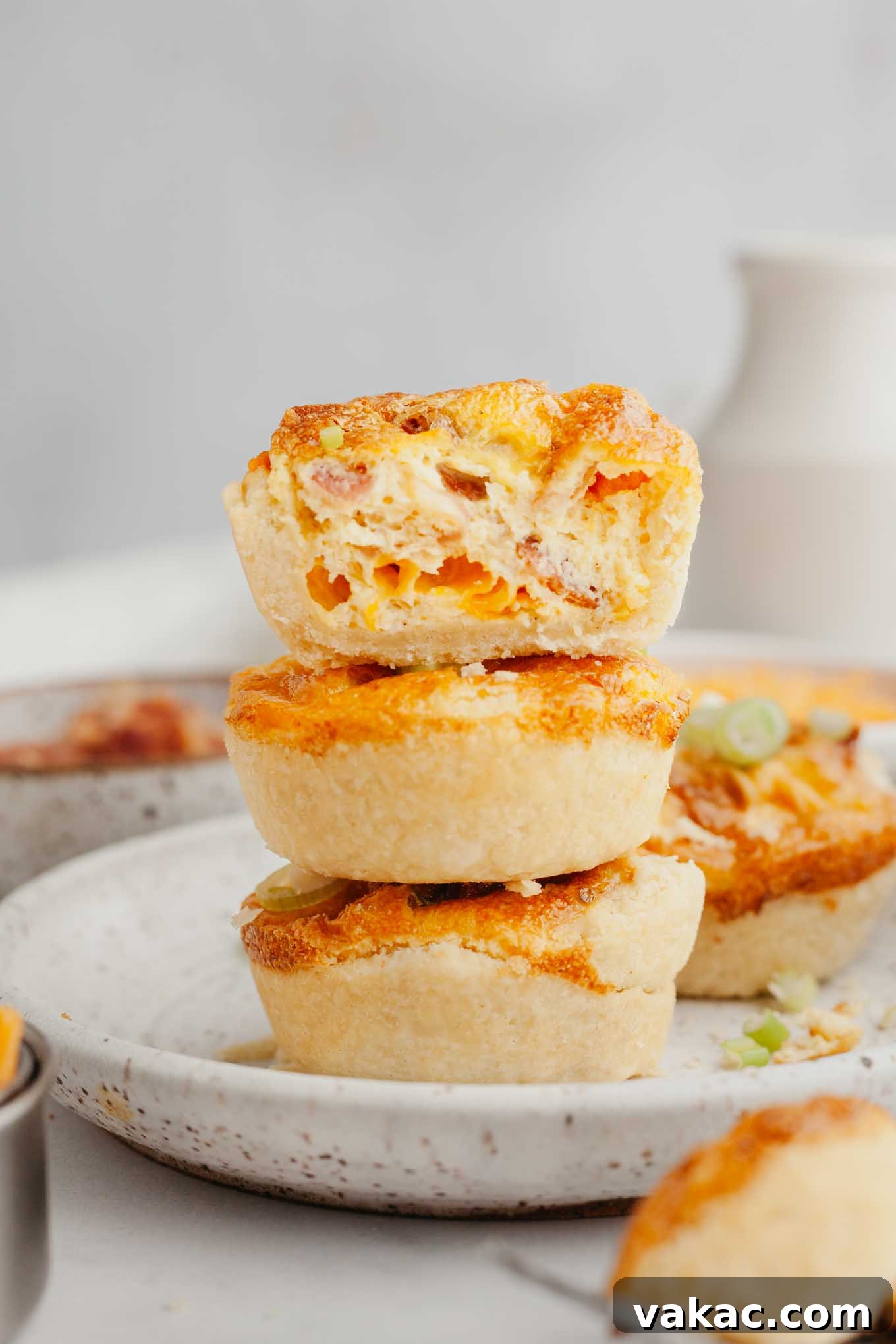 Bite-Sized Quiche Delights 11 A stack of three perfectly golden bite-sized quiches on a speckled white plate, highlighting their appealing individual portions.