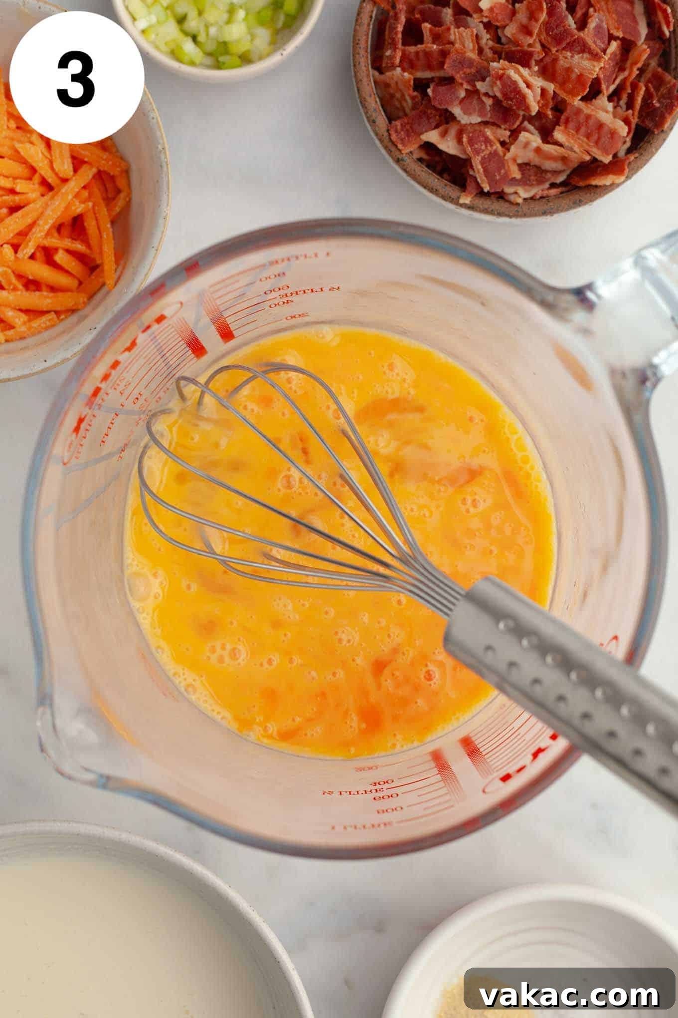 Bite-Sized Quiche Delights 6 An overhead view of beaten eggs in a clear measuring cup, surrounded by bowls of quiche mix-ins, prepared for the filling.
