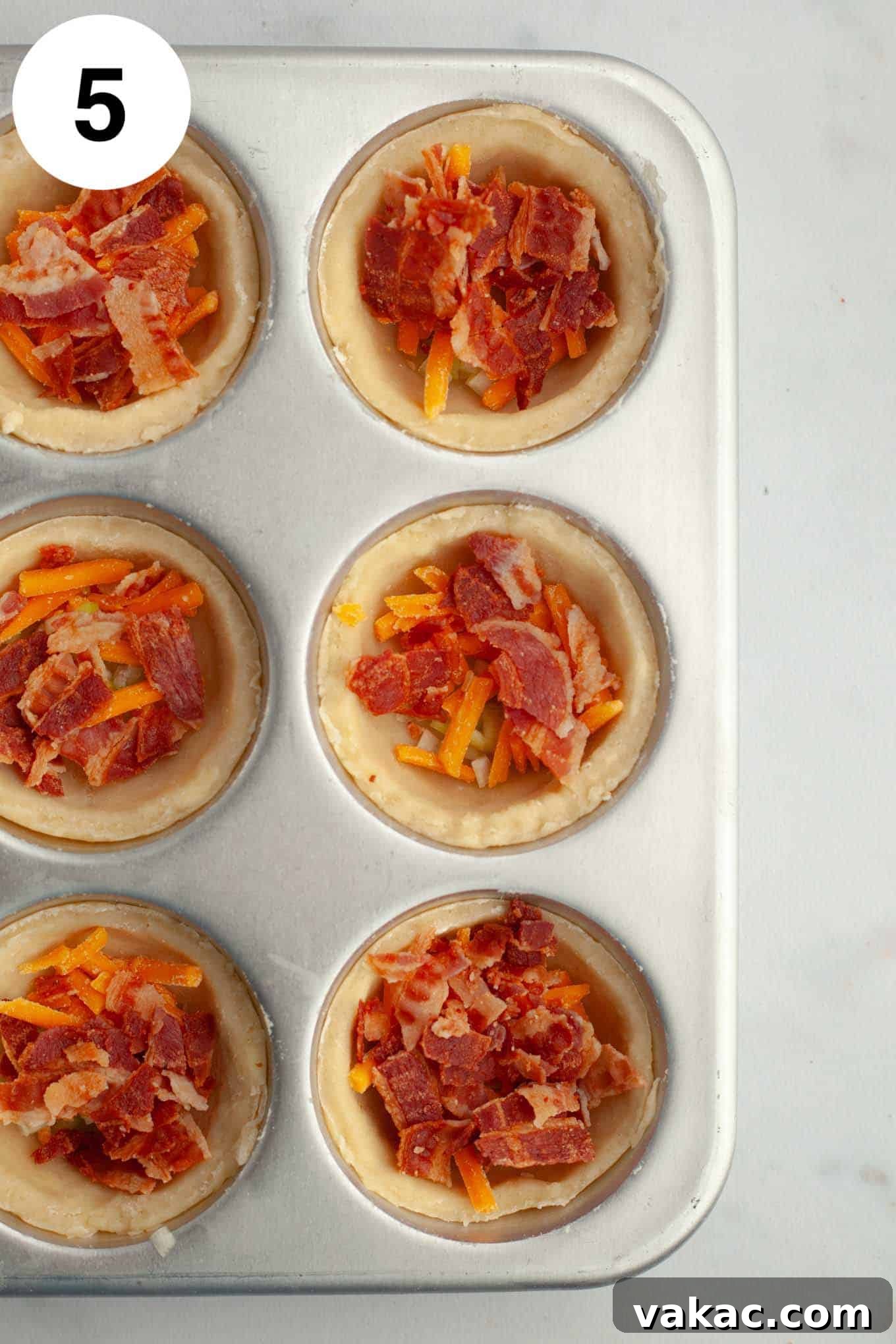 Bite-Sized Quiche Delights 8 An overhead view of partially filled mini quiches in a muffin pan, with mix-ins at the bottom and some egg mixture poured over.