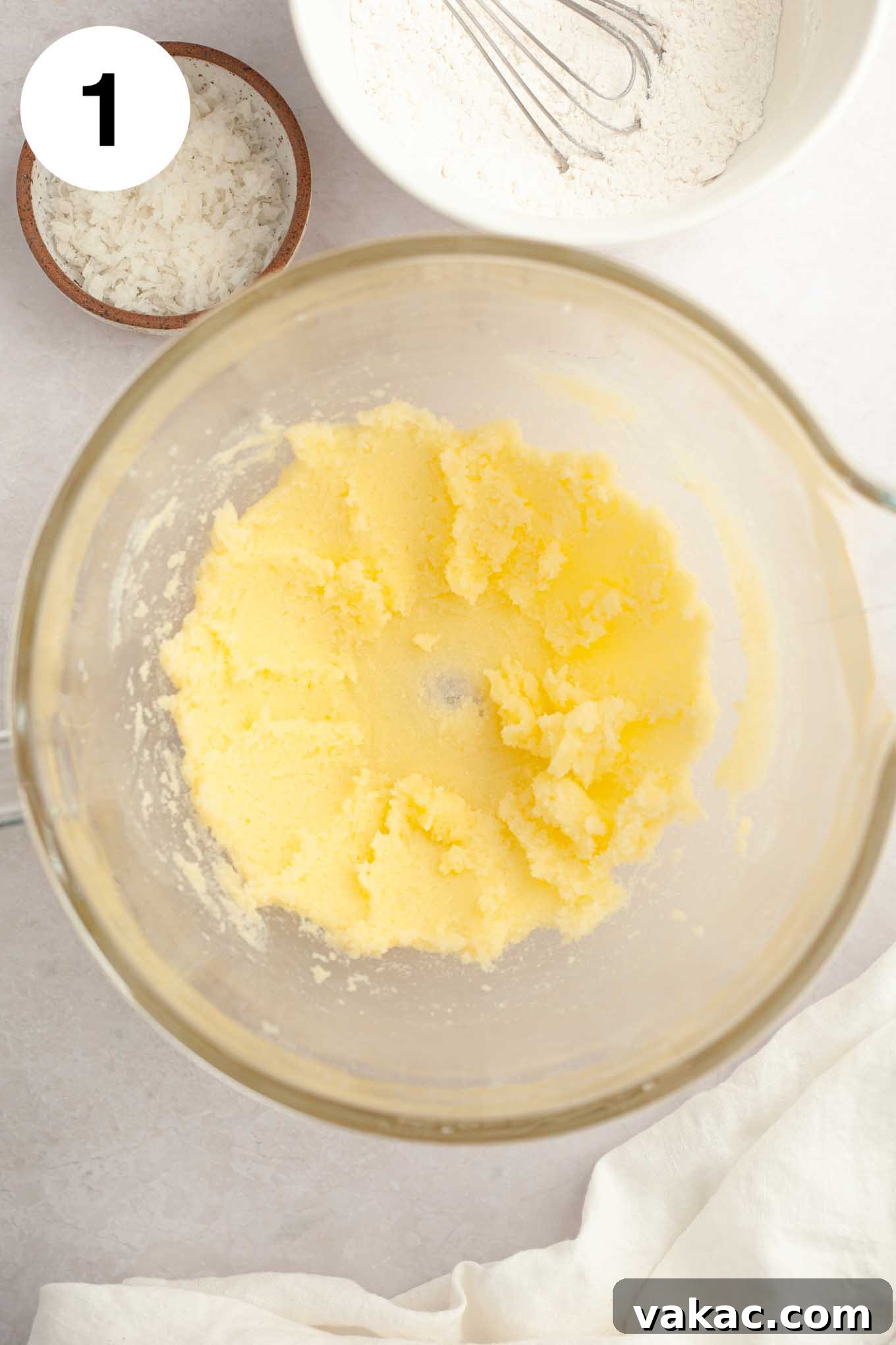 Tropical Coconut Delights 5 An overhead view of softened butter and granulated sugar perfectly creamed together in a clear glass mixing bowl, forming a light and airy mixture.