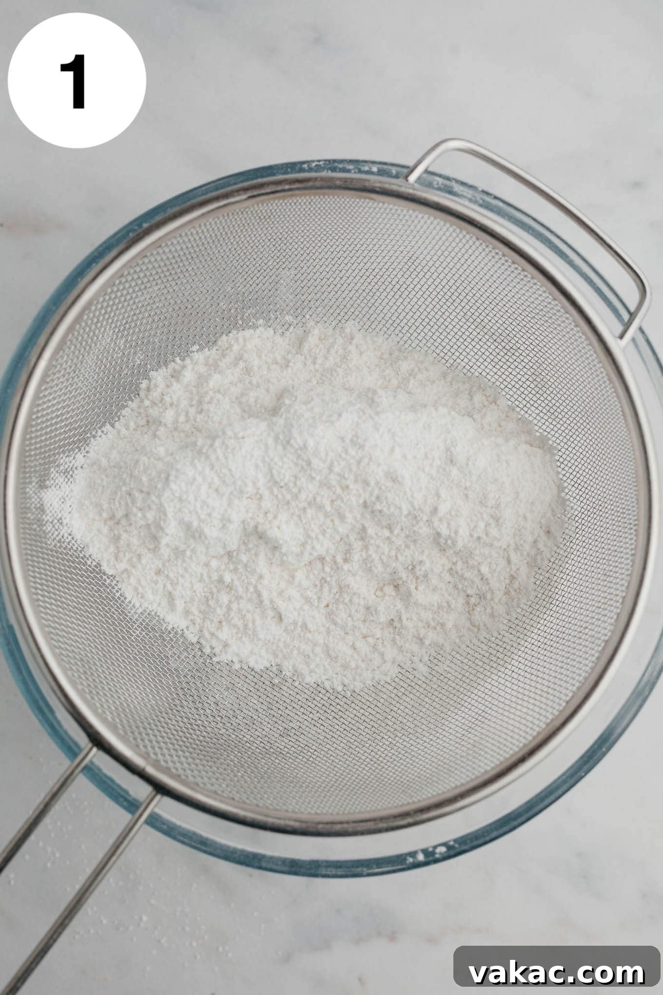 Cloud-Light Cupcakes 4 An overhead view of flour and powdered sugar in a fine mesh sieve over a mixing bowl.