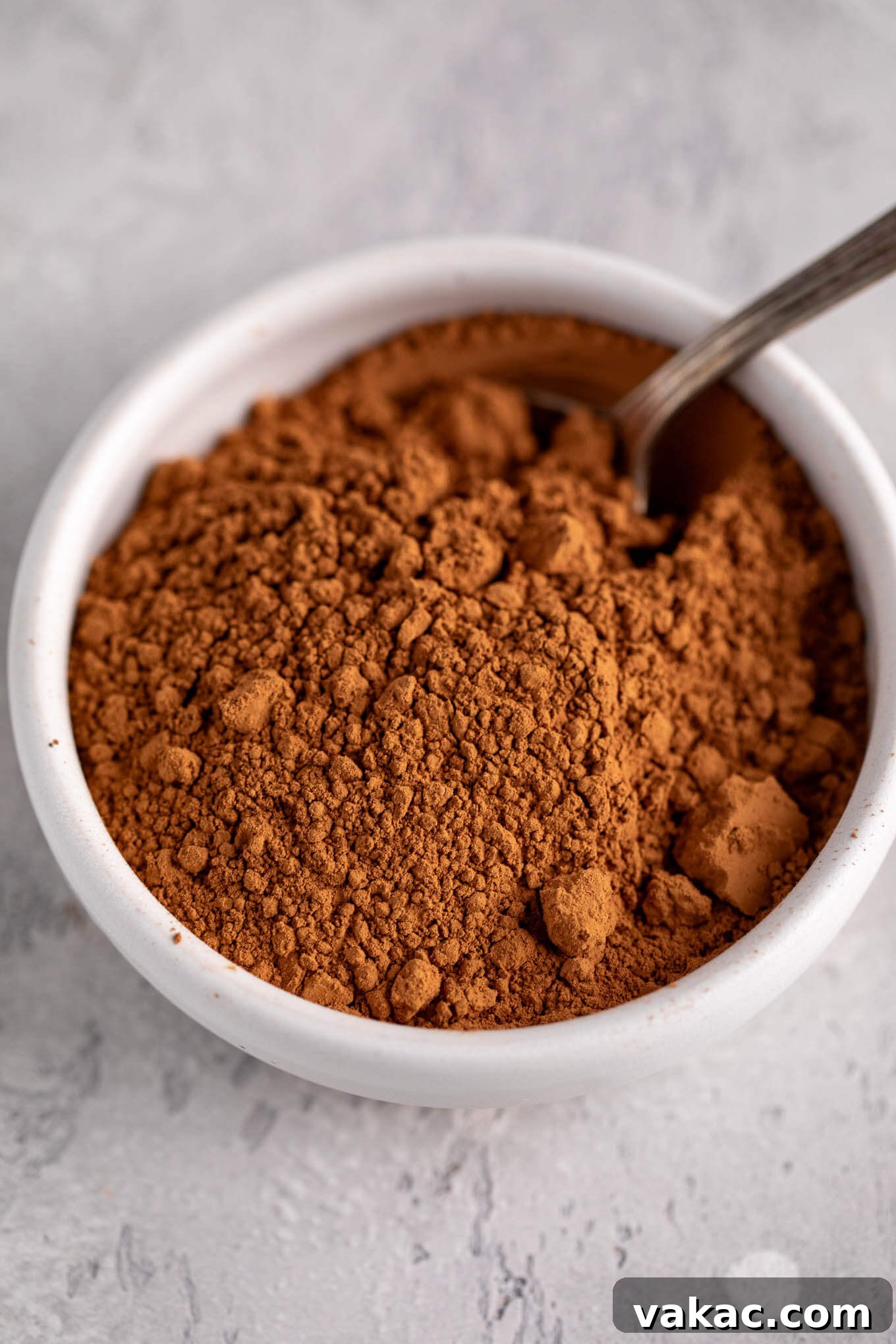 Natural vs. Dutch Process Cocoa: The Baker's Choice 4 Brightly colored natural cocoa powder presented in a white ceramic bowl with a small silver spoon.
