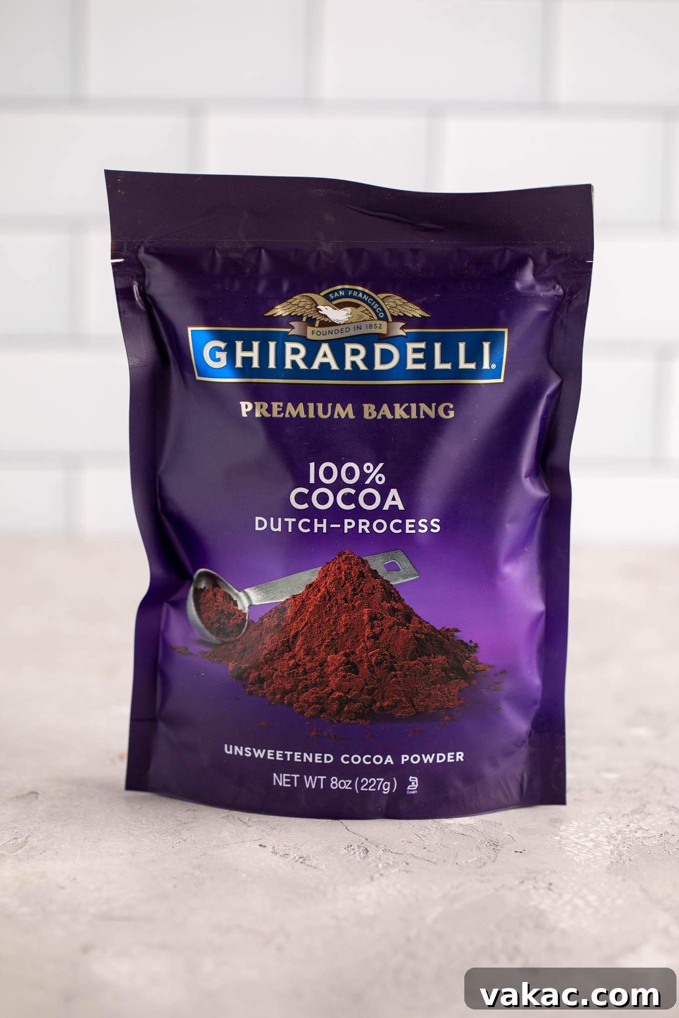 Natural vs. Dutch Process Cocoa: The Baker's Choice 5 A dark package of Ghirardelli Dutch process cocoa powder rests on a neutral gray surface, showcasing its rich appearance.