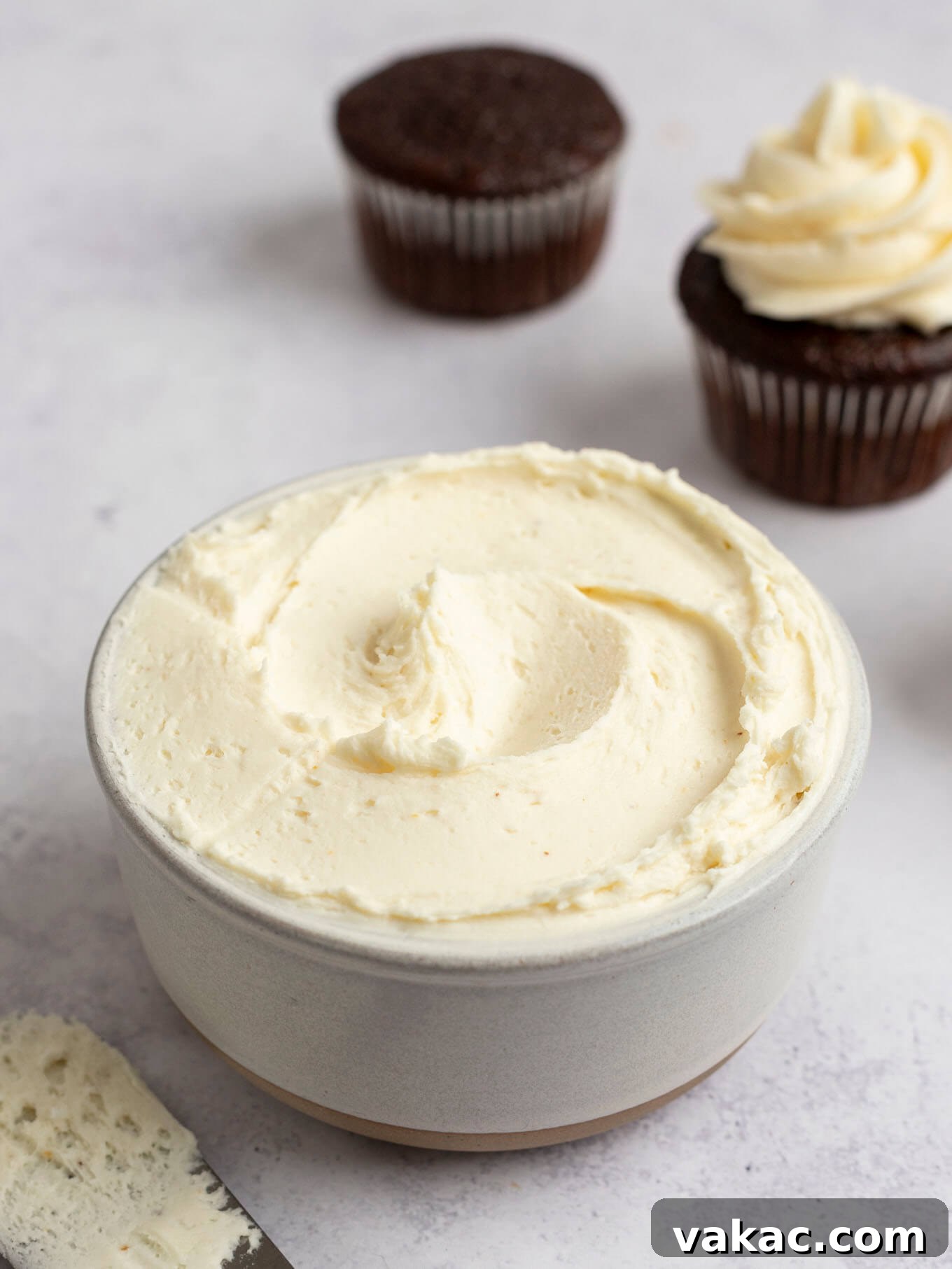 Caramelized Buttercream Dream 10 Brown butter frosting in a white bowl, with two chocolate cupcakes sitting nearby, ready to be frosted.
