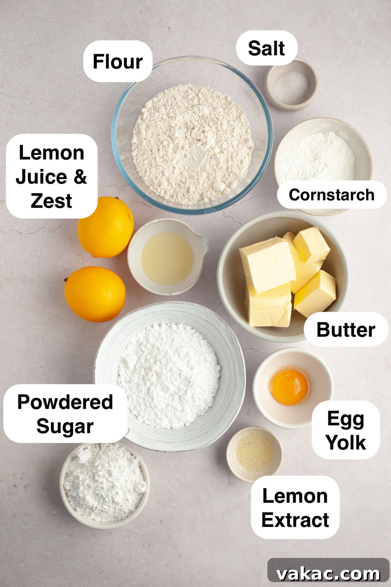 An overhead view of the fresh ingredients needed for baking lemon meltaway cookies, including lemons, butter, eggs, and various baking essentials laid out on a clean surface.