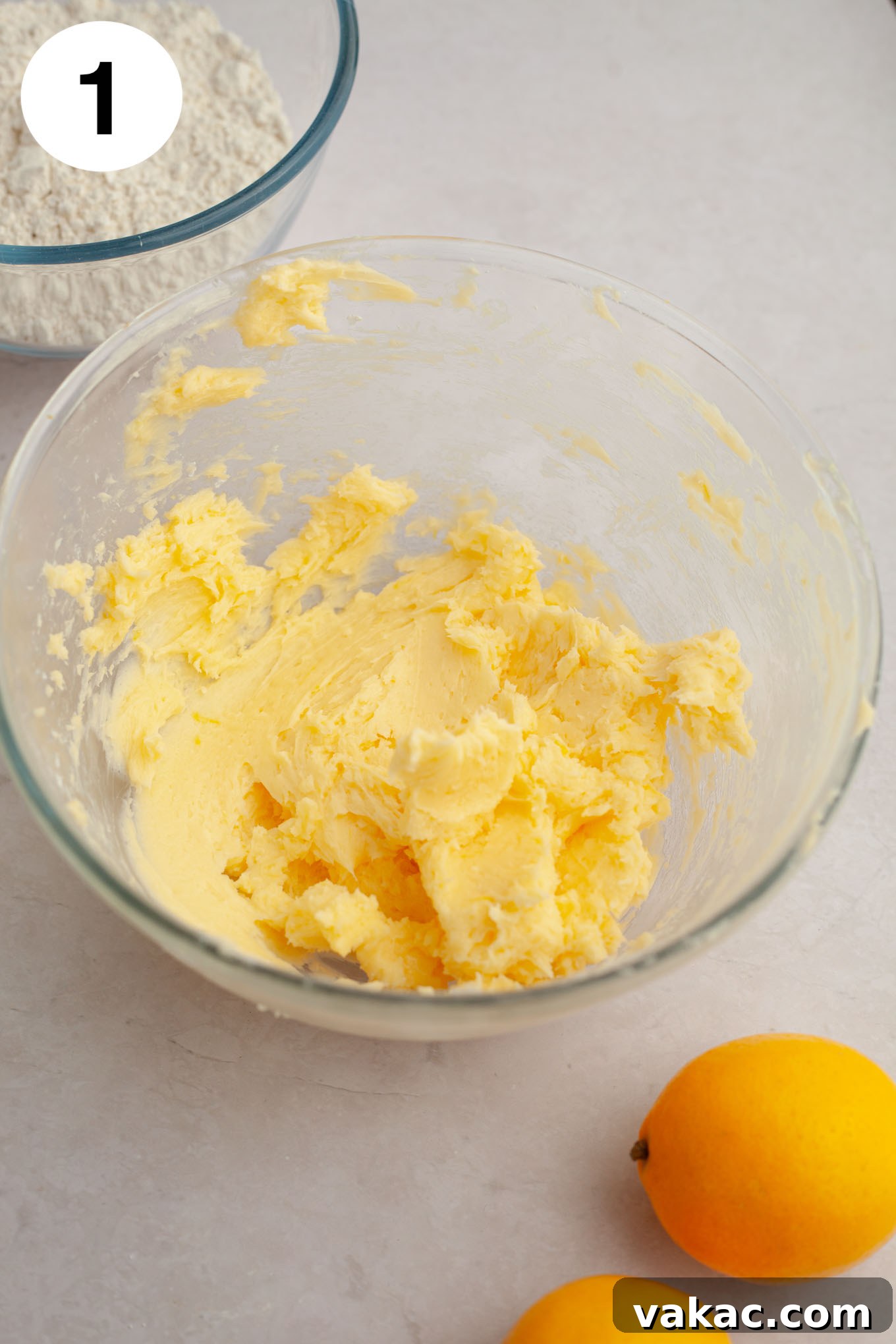 An overhead view of creamed butter, powdered sugar, egg yolk, and fresh lemon zest and juice combined in a clear glass mixing bowl, ready for further mixing.