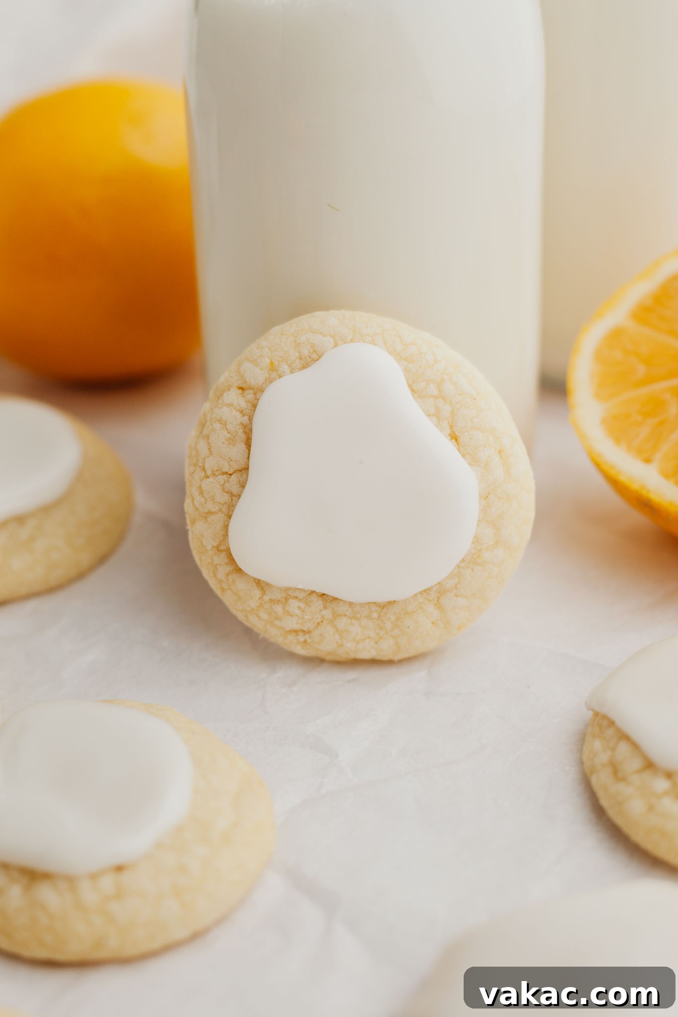 A perfectly glazed lemon meltaway cookie, propped casually against a small, rustic jug of milk, showcasing its delicate texture and bright icing.