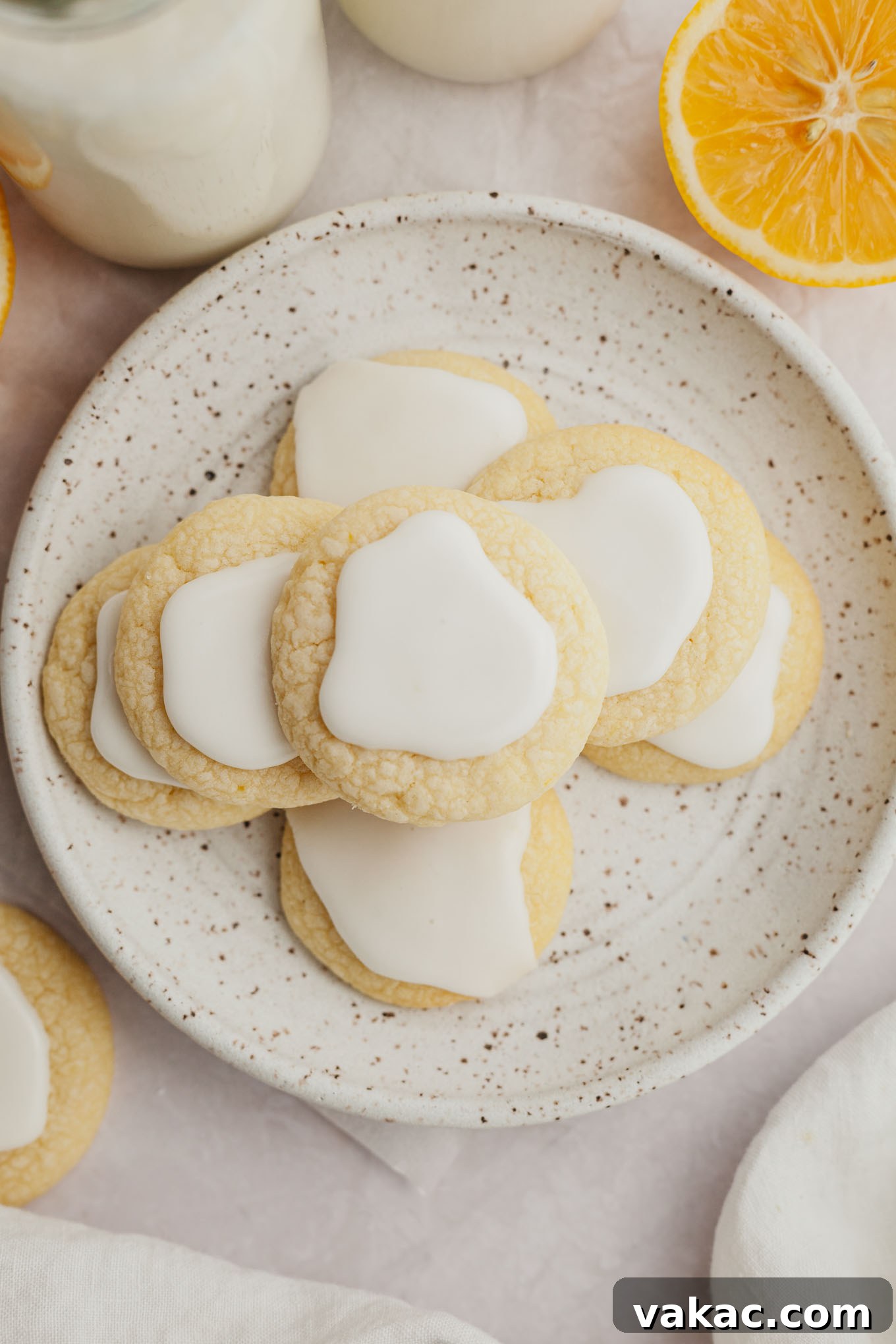 An overhead shot of a stack of lemon meltaway cookies with glossy lemon icing, presented beautifully on a white speckled plate.