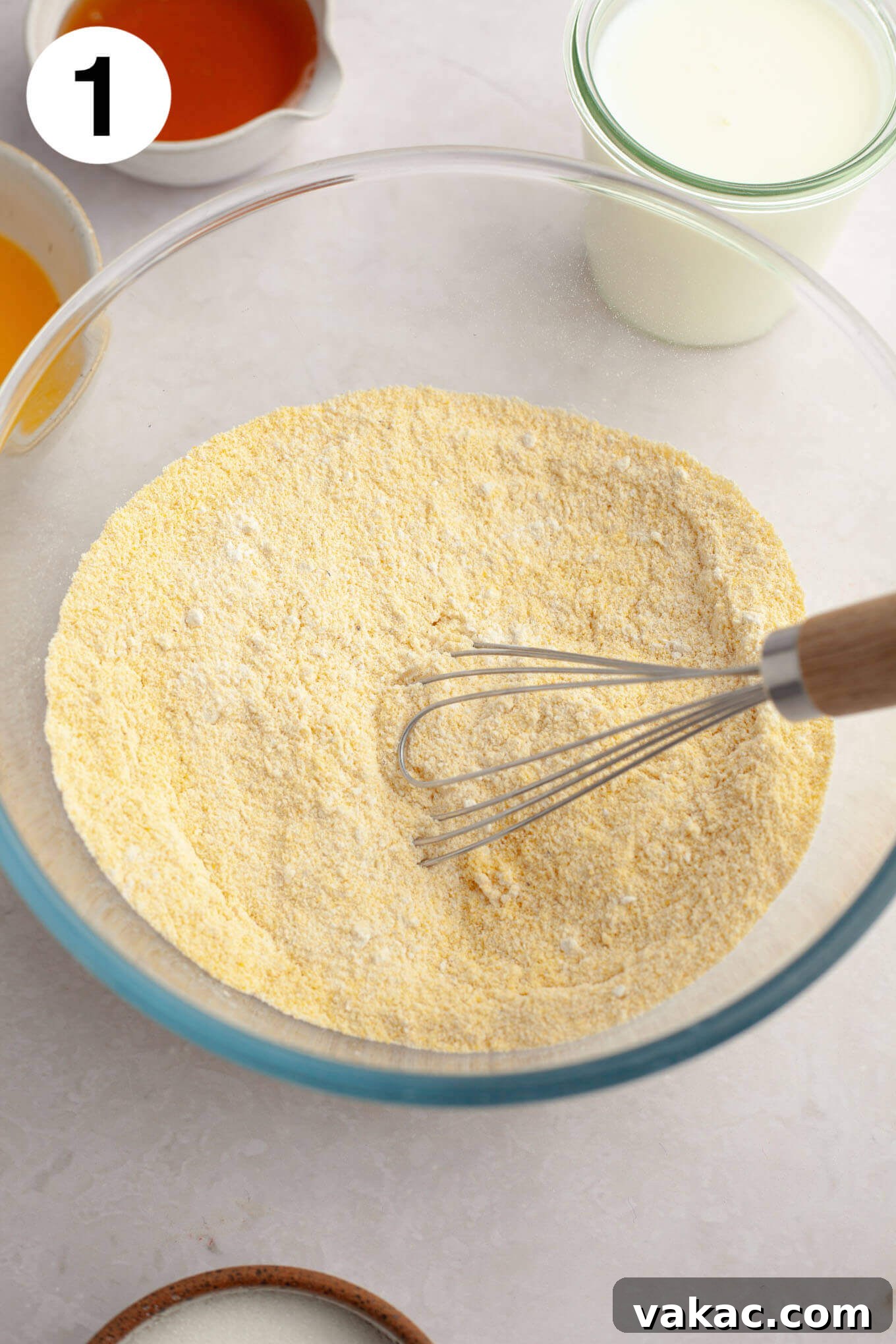 Golden Fluffy Cornbread Muffins 4 An overhead view of the dry ingredients (flour, cornmeal, leavening) mixed together in a clear glass bowl, ready for the wet ingredients.