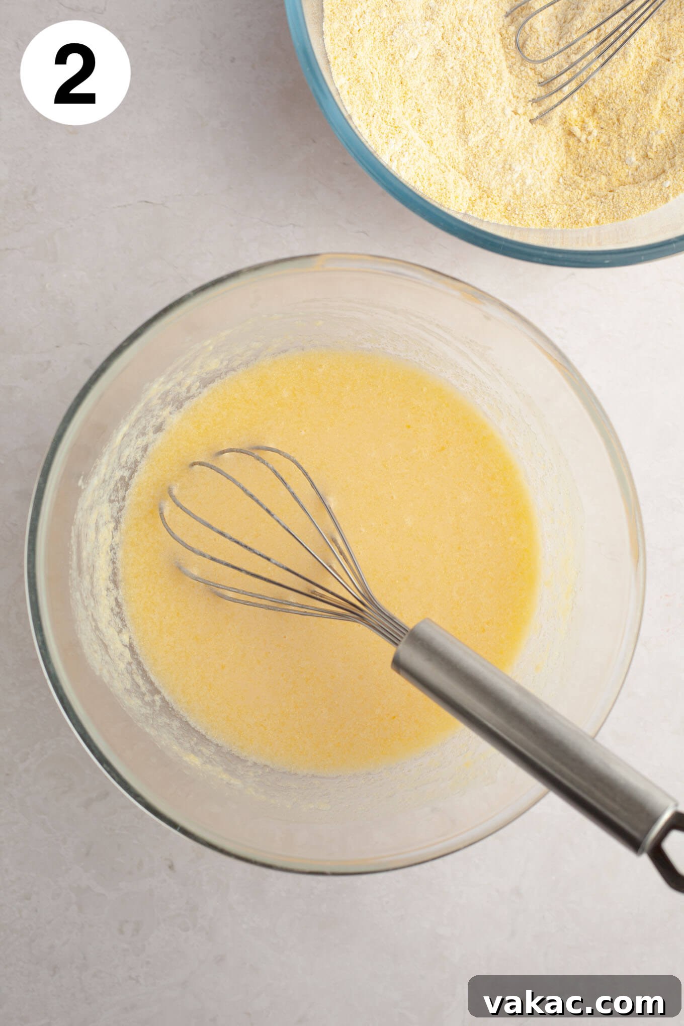 Golden Fluffy Cornbread Muffins 5 An overhead view of the wet ingredients for cornbread muffins (melted butter, sugar, honey, eggs, buttermilk) being whisked in a glass mixing bowl.