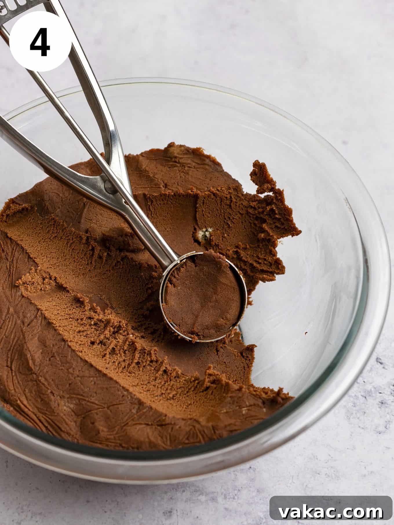 Chilled cookie dough in a glass mixing bowl, with a cookie scoop positioned beside it, ready for portioning.