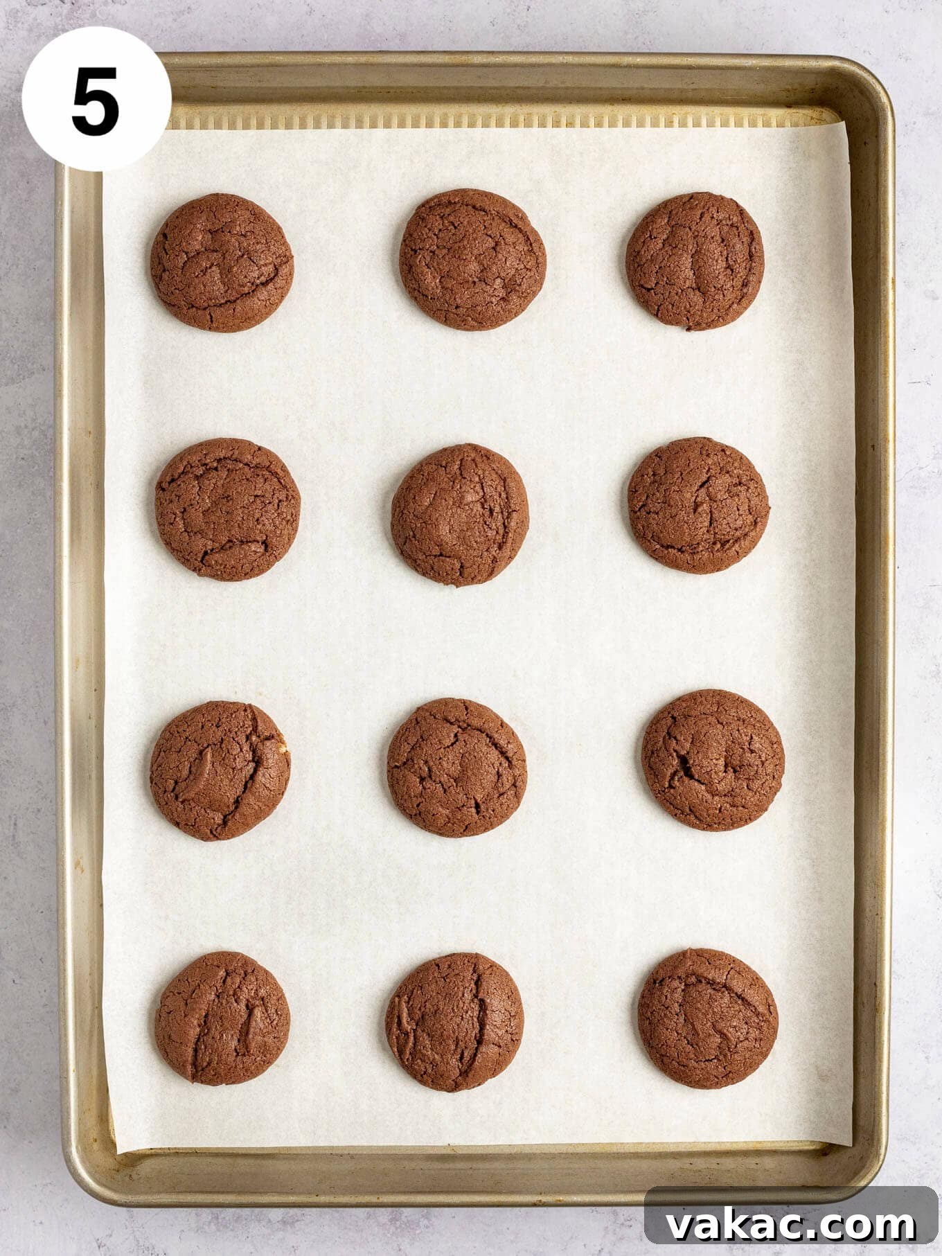 An overhead shot of freshly baked chocolate cookies arranged on a baking sheet lined with parchment paper.