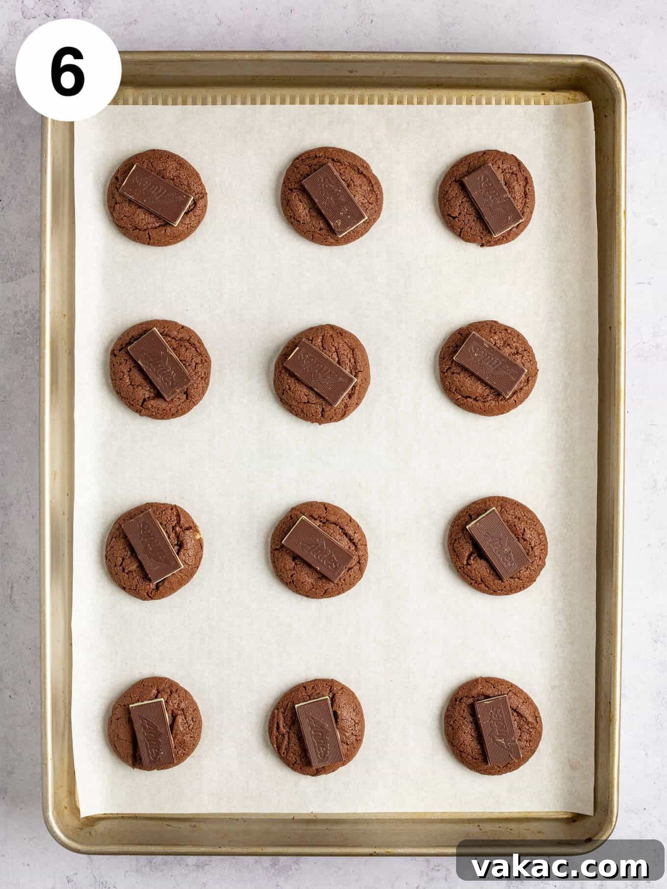 An overhead view of warm, baked chocolate cookies, each topped with a melting Andes mint, on a baking sheet.