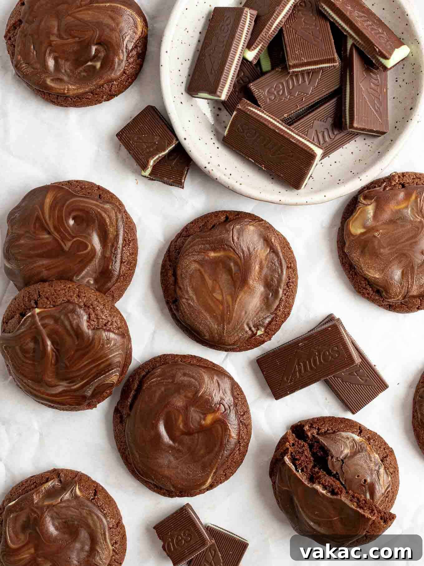 An overhead view of several finished Andes mint cookies beautifully spread out on parchment paper, with a bowl of unwrapped Andes mints nearby.
