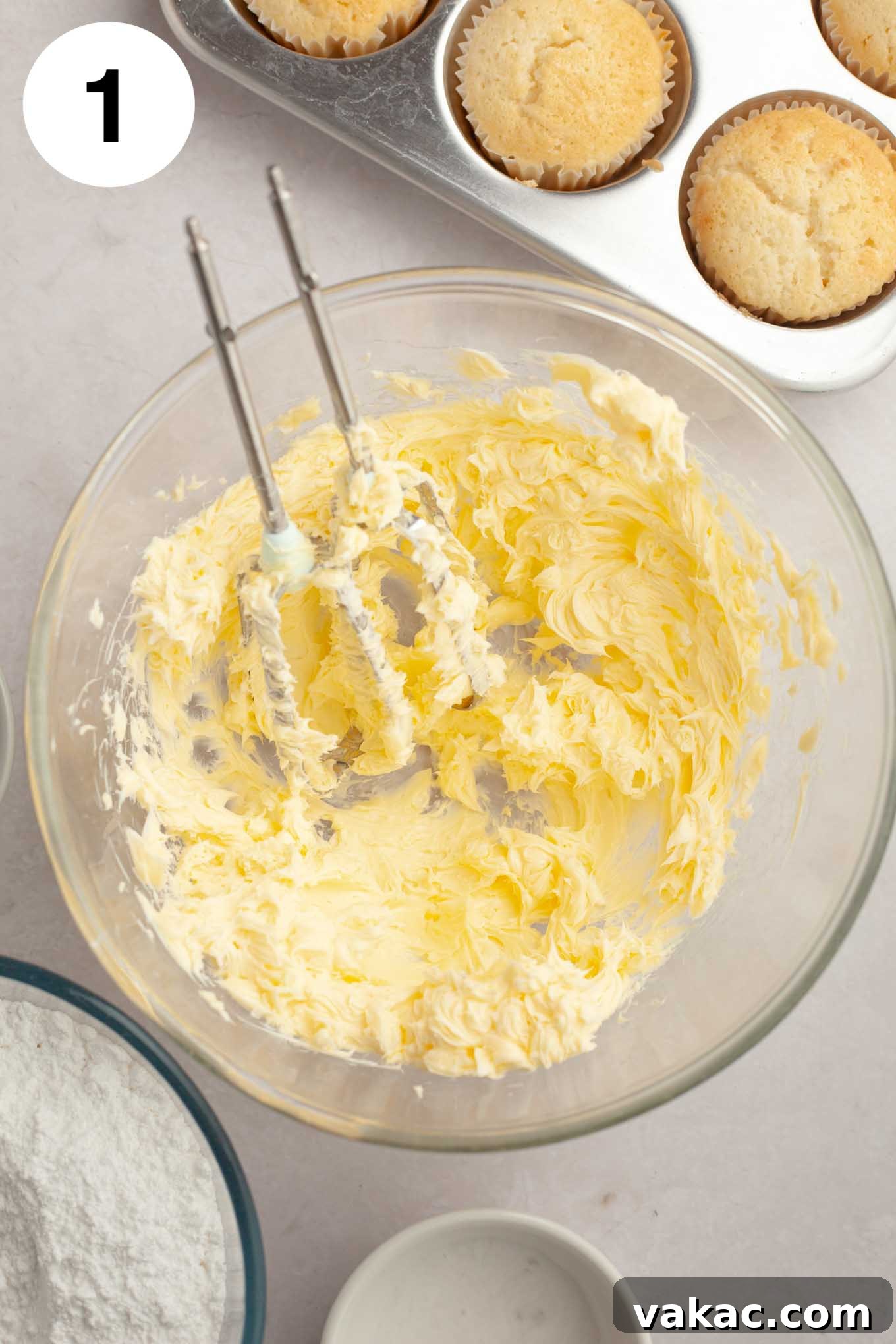 A glass mixing bowl holds beautifully creamed, smooth, and pale yellow softened butter, ready for the next step in making coconut frosting.