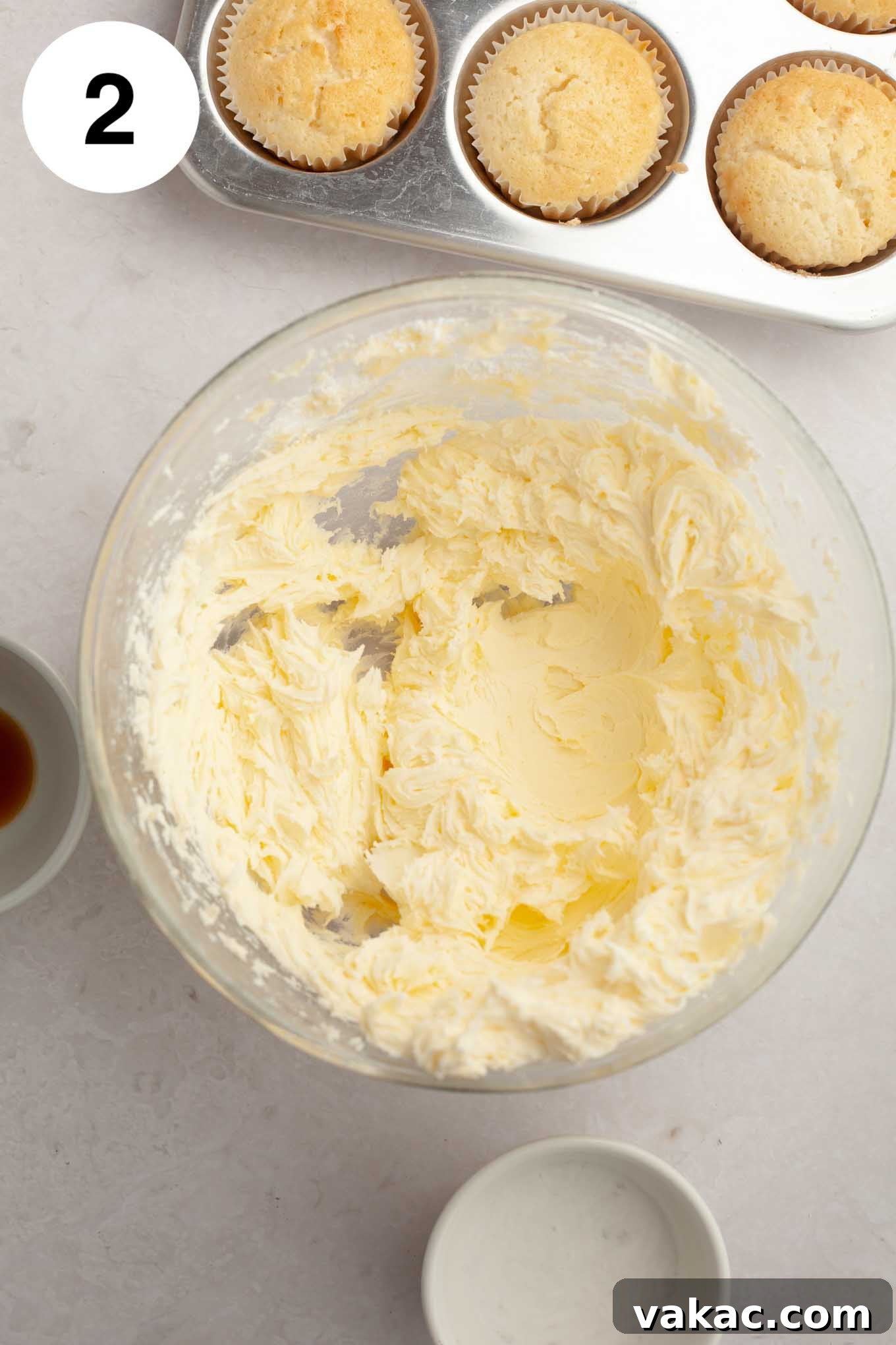 Inside a glass mixing bowl, softened butter and powdered sugar are partially combined, creating a thick, crumbly, and slightly creamy mixture.