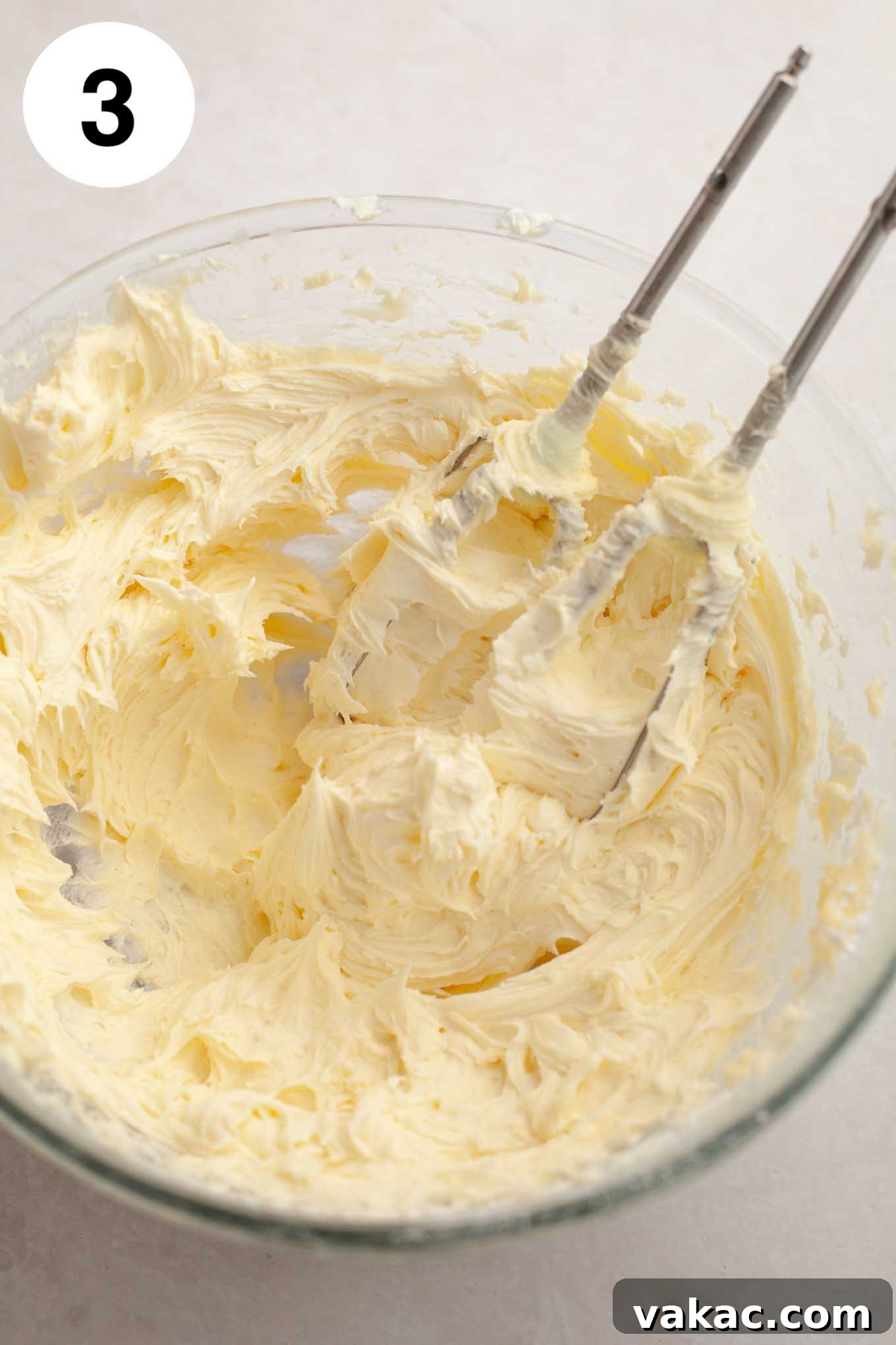 A glass mixing bowl filled with freshly made, velvety smooth coconut frosting, displaying its creamy white texture, ready for use.