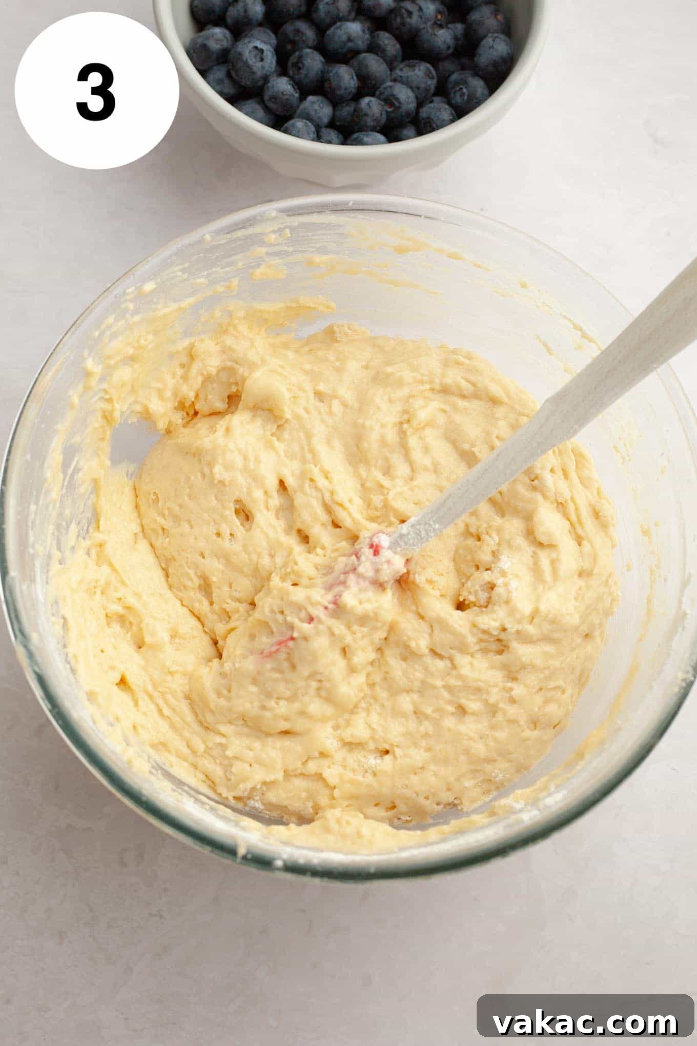 Berry Burst Bread 6 An overhead view of smooth quick bread batter in a clear glass mixing bowl, showcasing its light and airy texture before the addition of blueberries.