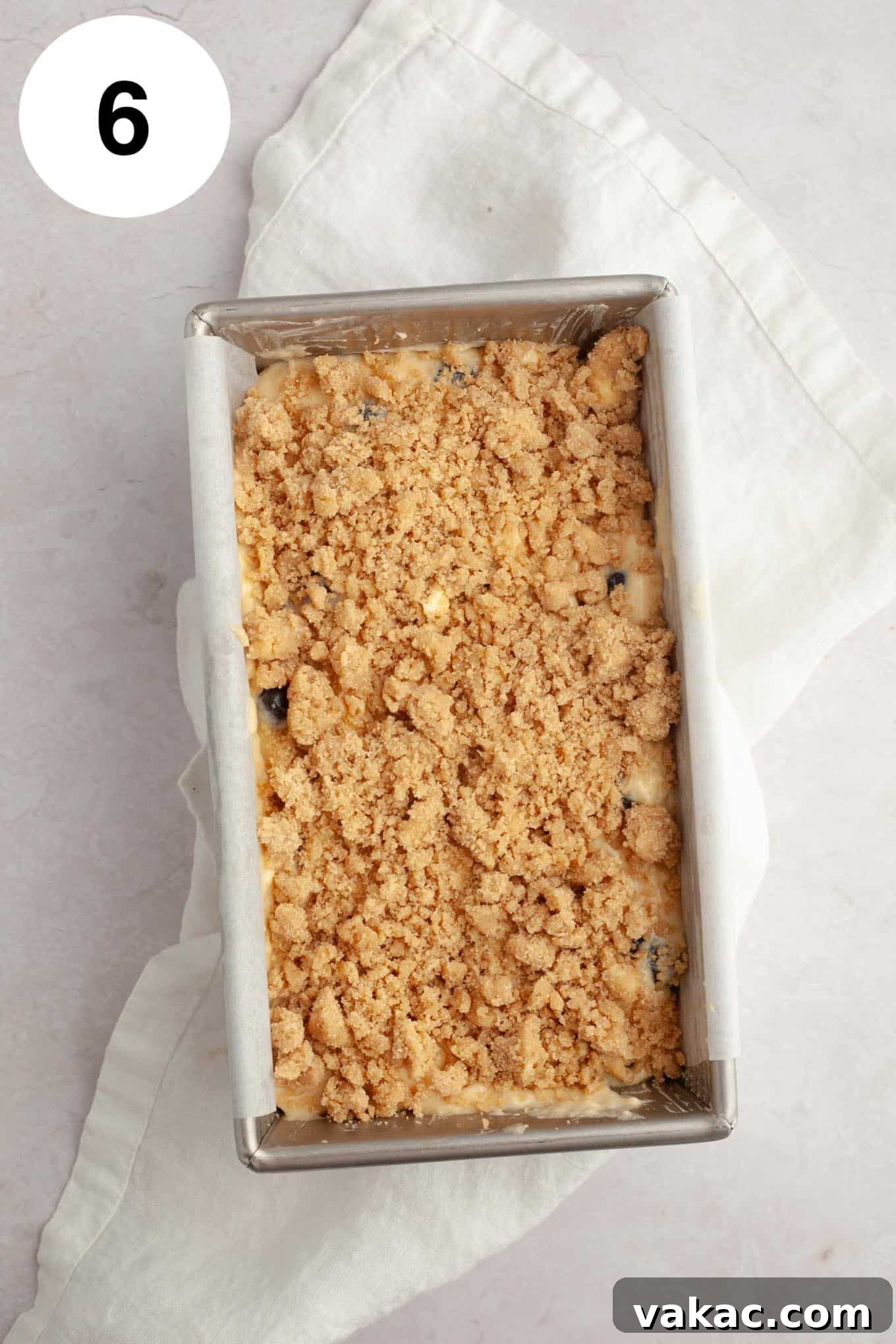 Berry Burst Bread 9 An overhead view of an unbaked blueberry loaf in a parchment-lined pan, generously topped with a golden cinnamon streusel, perfectly prepared and ready to be placed in the oven.
