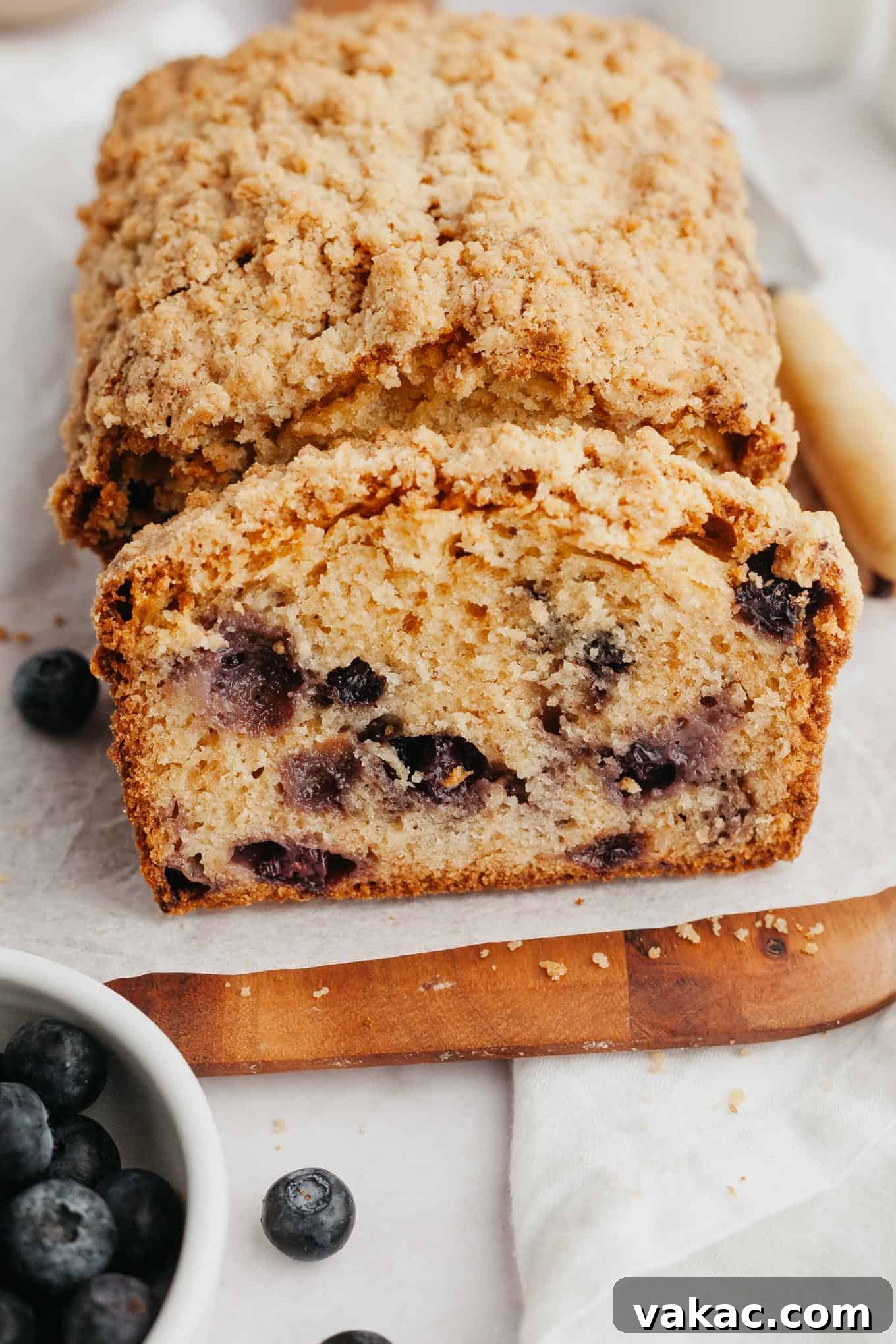 Berry Burst Bread 10 A close-up view of a perfectly sliced loaf of moist blueberry bread, beautifully revealing the even distribution of plump blueberries throughout the tender crumb and the irresistible golden, crumbly streusel topping.