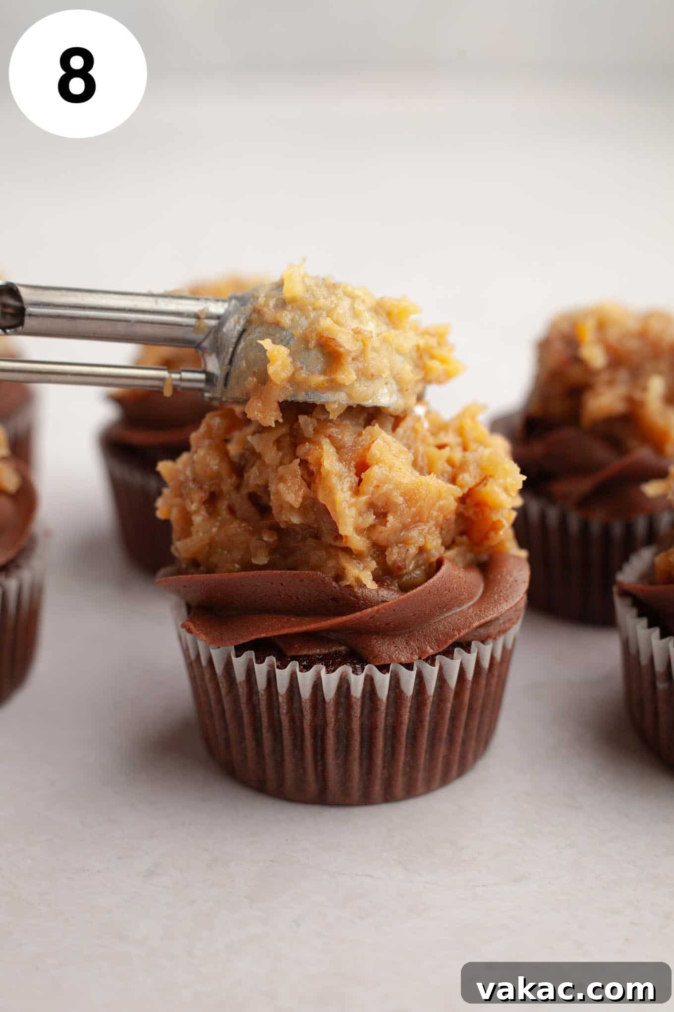Ultimate German Chocolate Cupcakes 12 A process shot showing German chocolate frosting being dolloped onto chocolate cupcakes.