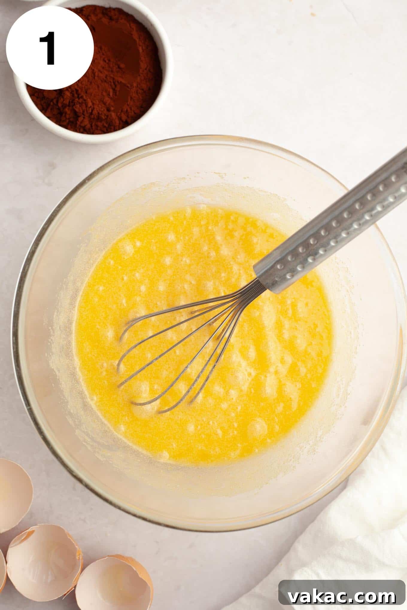 An overhead view of melted butter and sugar in a glass mixing bowl, with a whisk. 