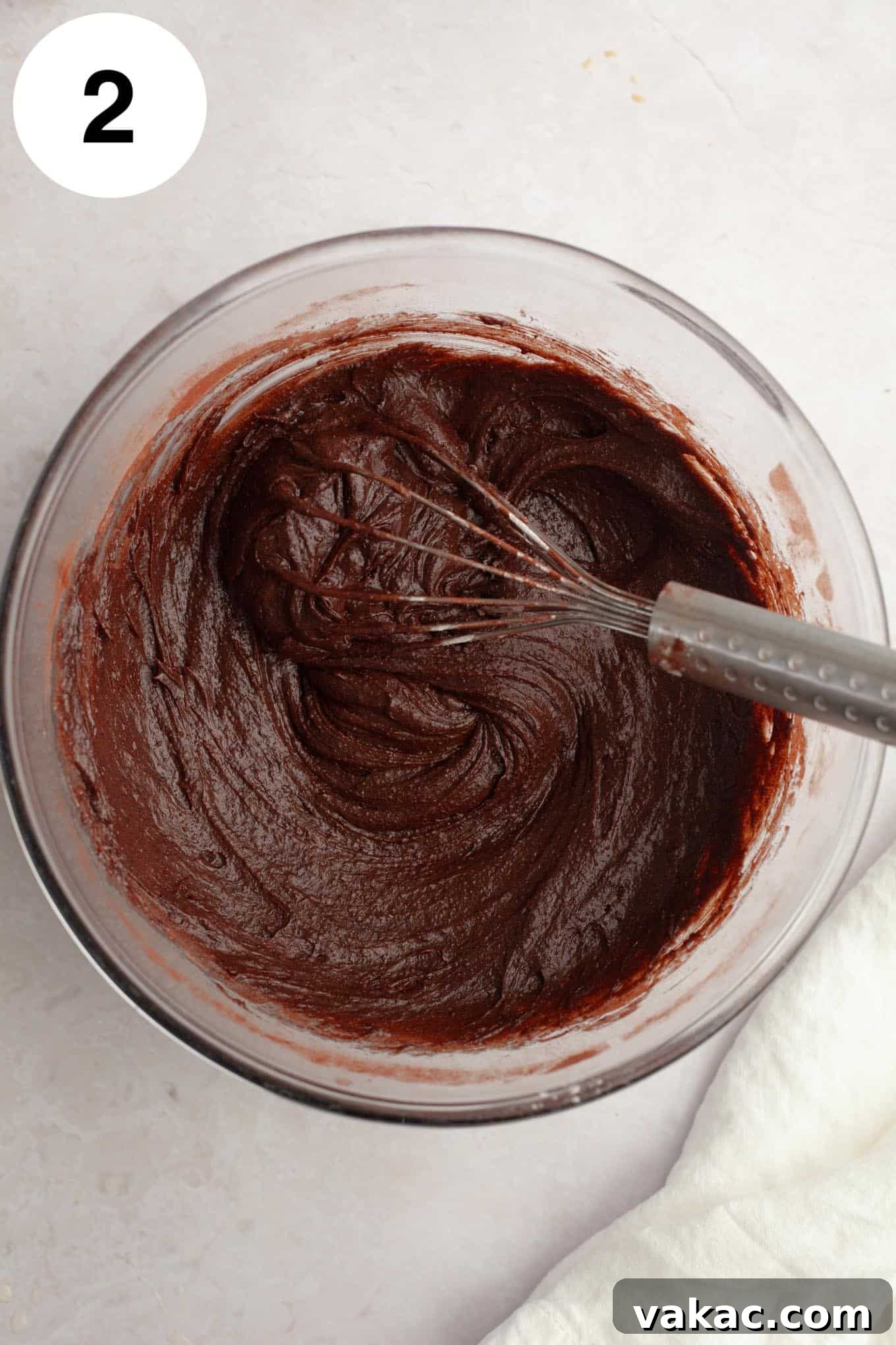 An overhead view of brownie batter in a glass mixing bowl, with a whisk. 