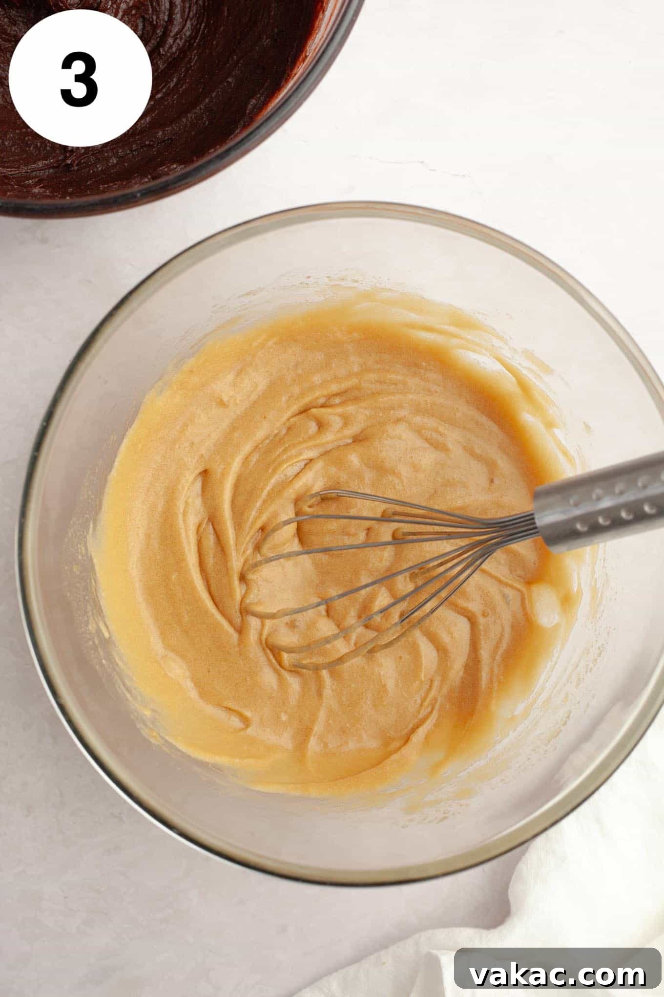 An overhead view of melted butter, eggs, and sugar in a glass mixing bowl, with a whisk. 