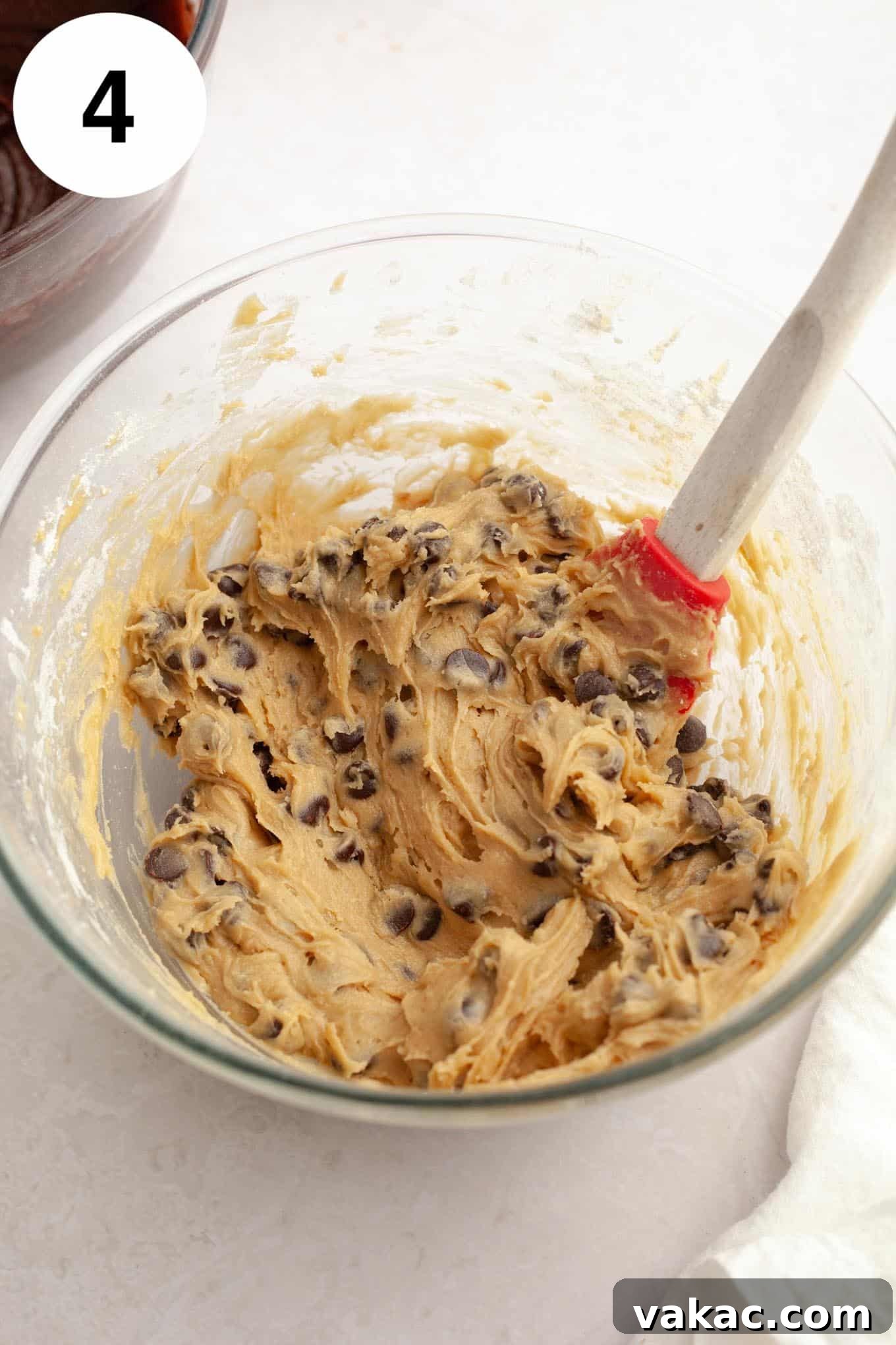 An overhead view of chocolate chip cookie dough in a glass mixing bowl, with a whisk. 