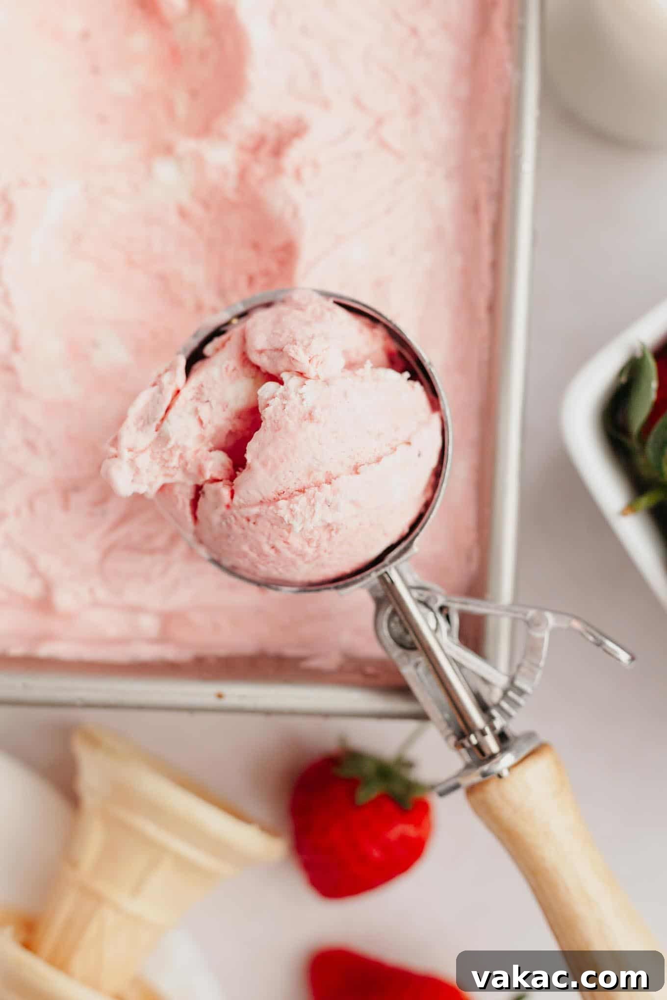 Strawberry Dream Cream 11 A perfectly scooped ball of strawberry ice cream held aloft by an ice cream scoop, with a pan of more ice cream visible below, ready to be enjoyed.