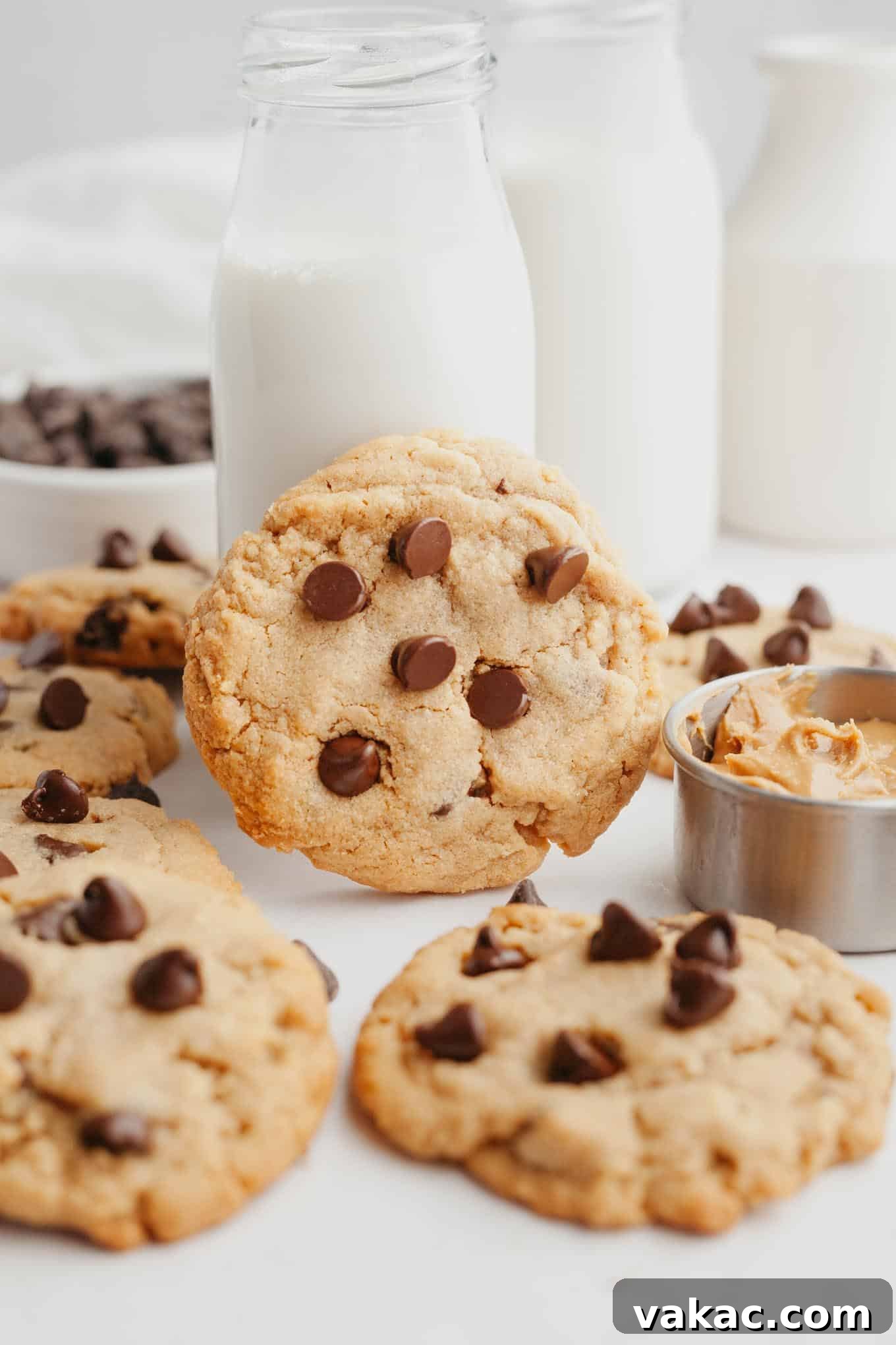 Peanut Butter Chocolate Bliss Bites 11 A single, inviting peanut butter chocolate chip cookie leans against a charming glass jug of milk, surrounded by more delectable cookies, creating a perfect snack tableau.