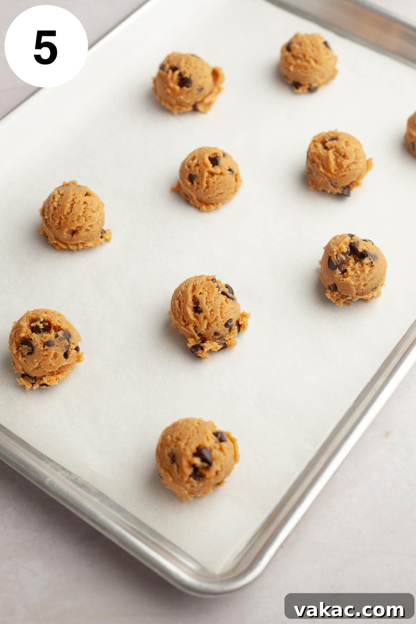 Peanut Butter Chocolate Bliss Bites 8 Uniform balls of peanut butter chocolate chip cookie dough, perfectly scooped and ready for baking, arranged on a parchment-lined baking sheet.