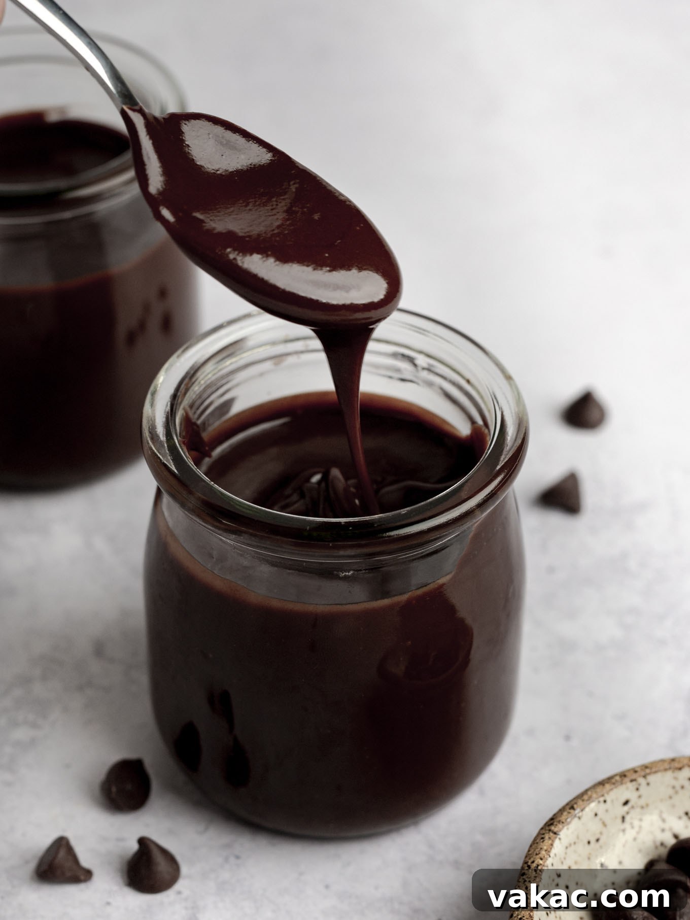 Decadent Homemade Hot Fudge Sauce 8 A spoonful of hot fudge sauce being held over a glass jar.