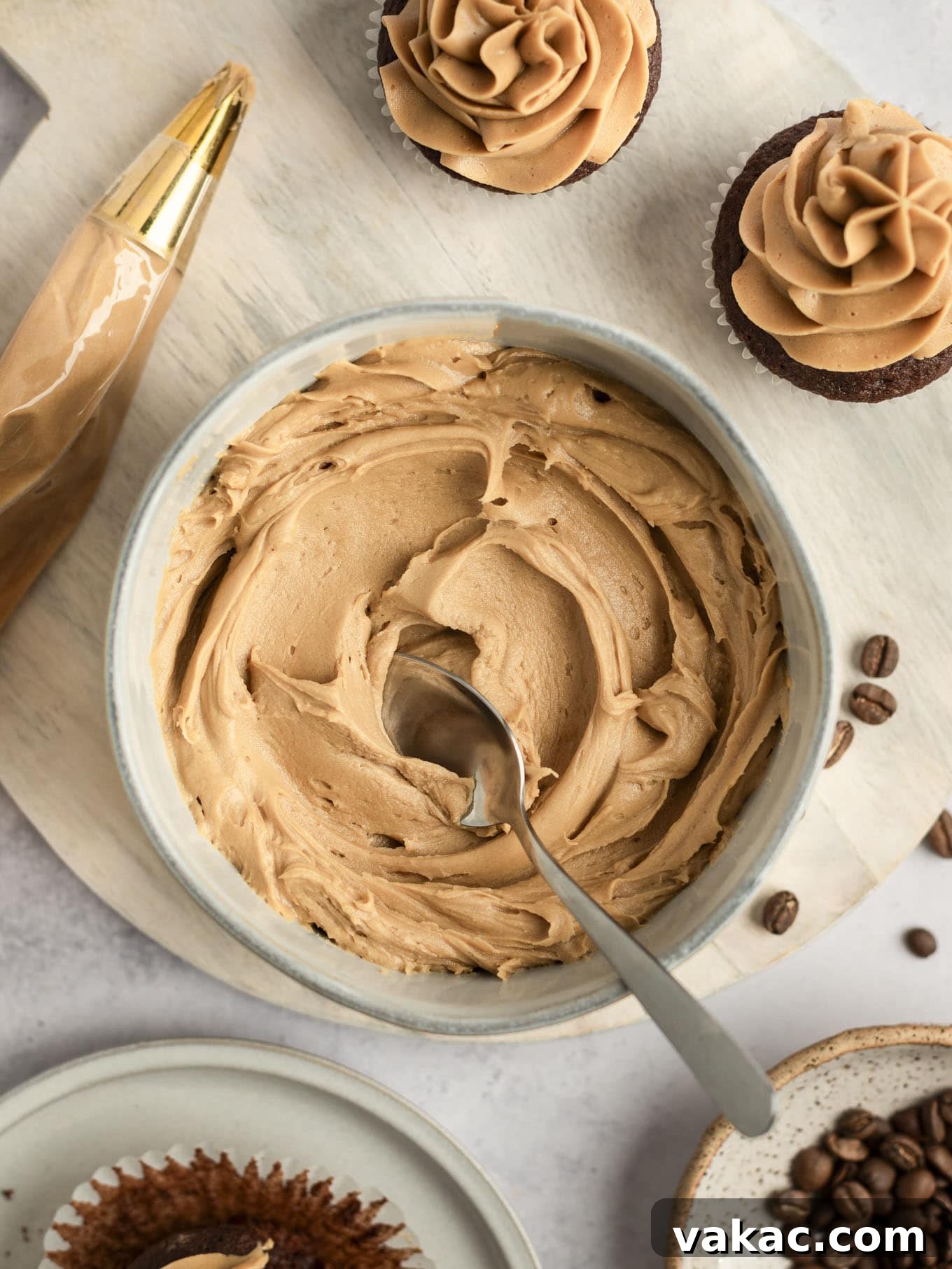 Java Dream Frost 2 An overhead view of a bowl of coffee buttercream frosting, with two decorated cupcakes, showcasing its creamy texture and rich color, inviting bakers to indulge.