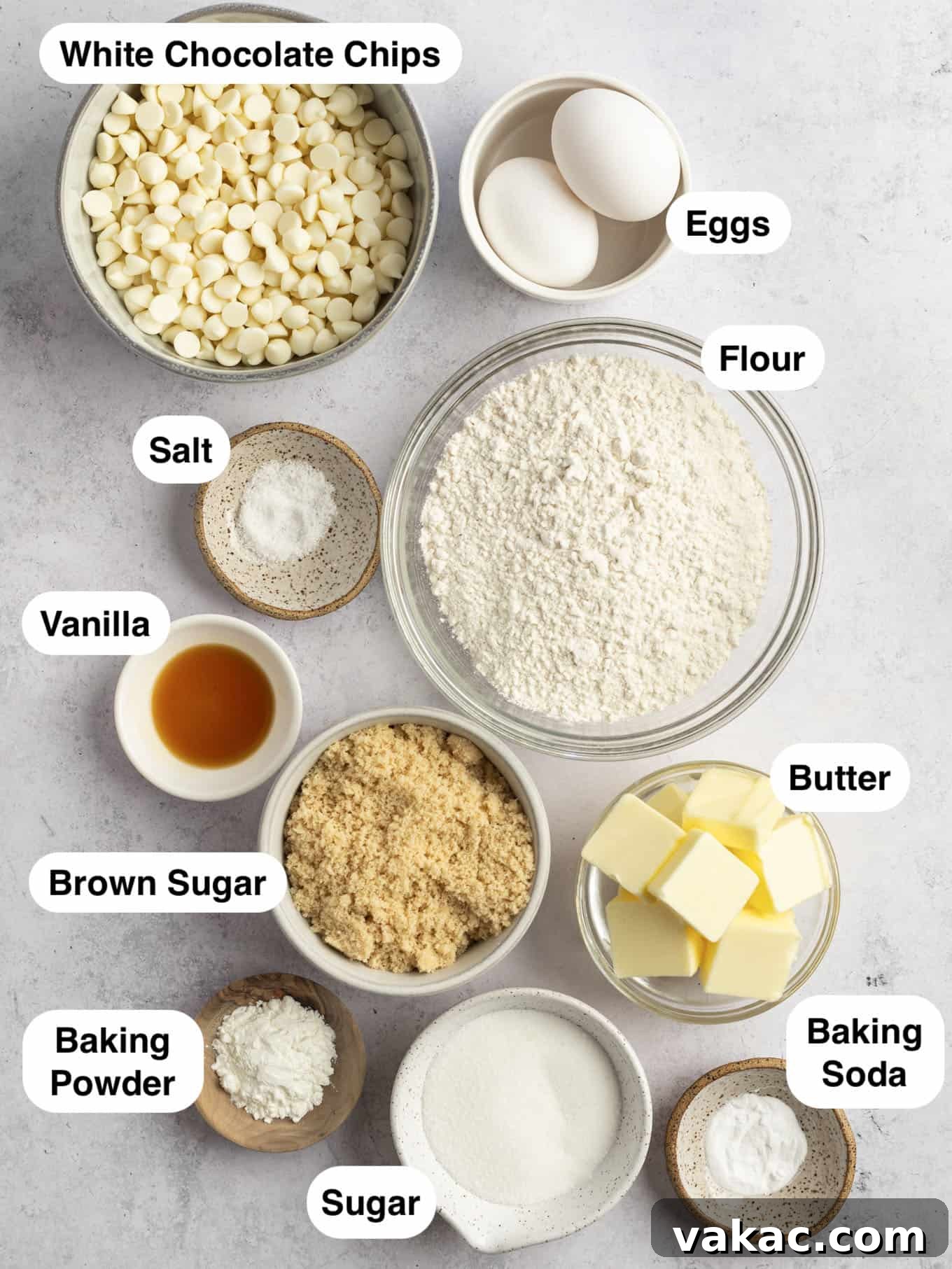 Irresistible White Chocolate Delights 3 An inviting overhead shot of key baking ingredients for making white chocolate chip cookies, including flour, brown and granulated sugars, eggs, softened butter, and a generous amount of white chocolate chips, neatly laid out on a clean counter surface, ready for preparation.