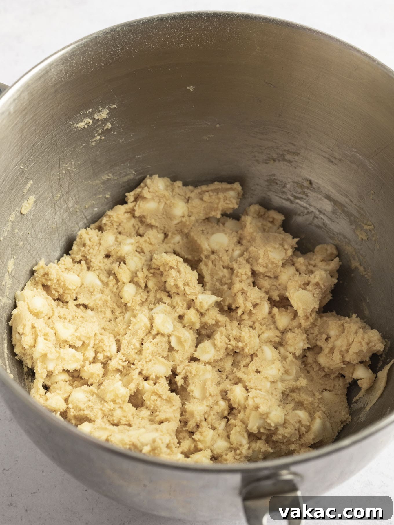 Irresistible White Chocolate Delights 5 A close-up view of white chocolate chip cookie dough in the bowl of a stand mixer, showing the uniform texture and evenly distributed white chocolate chips after all ingredients have been thoroughly mixed and incorporated.