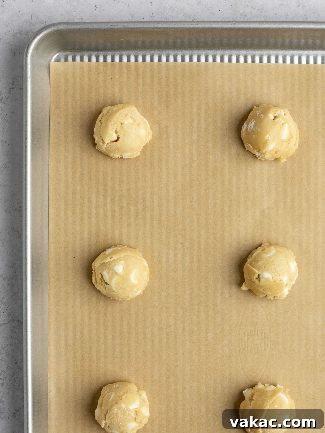 Irresistible White Chocolate Delights 6 Portions of white chocolate chip cookie dough perfectly scooped into uniform balls and arranged onto a baking sheet lined with brown parchment paper, ready for chilling or immediate baking.