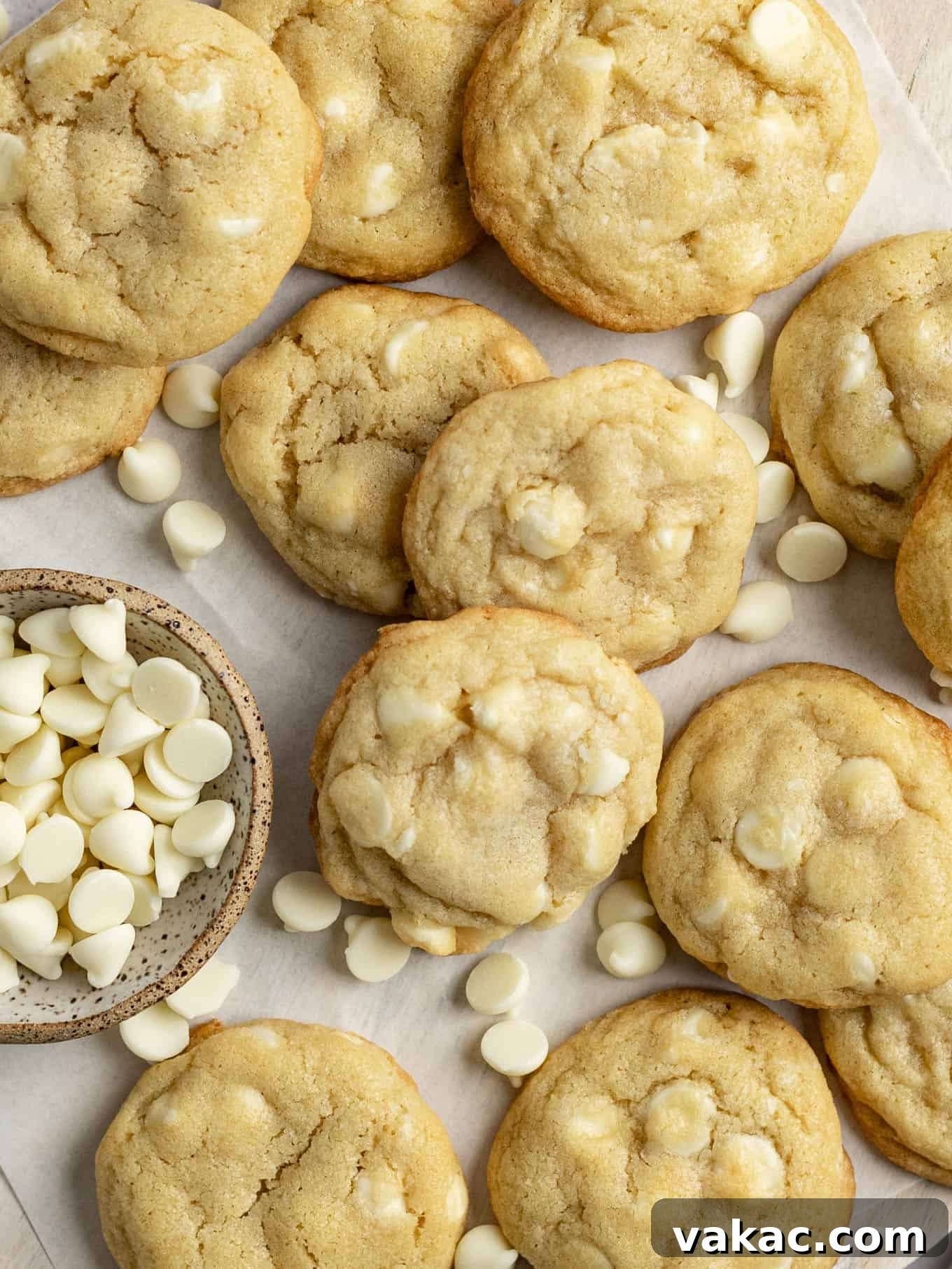 Irresistible White Chocolate Delights 7 An overhead shot of a batch of golden-brown white chocolate chip cookies cooling on parchment paper on a baking sheet, showcasing their perfect round shape, slightly crinkled tops, and scattered white chocolate pieces.